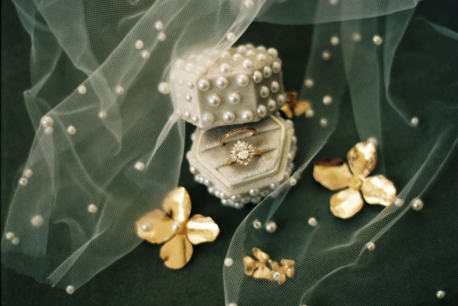 Delicate white tulle fabric adorned with pearl beads and gold floral accents creates an elegant bridal accessory.