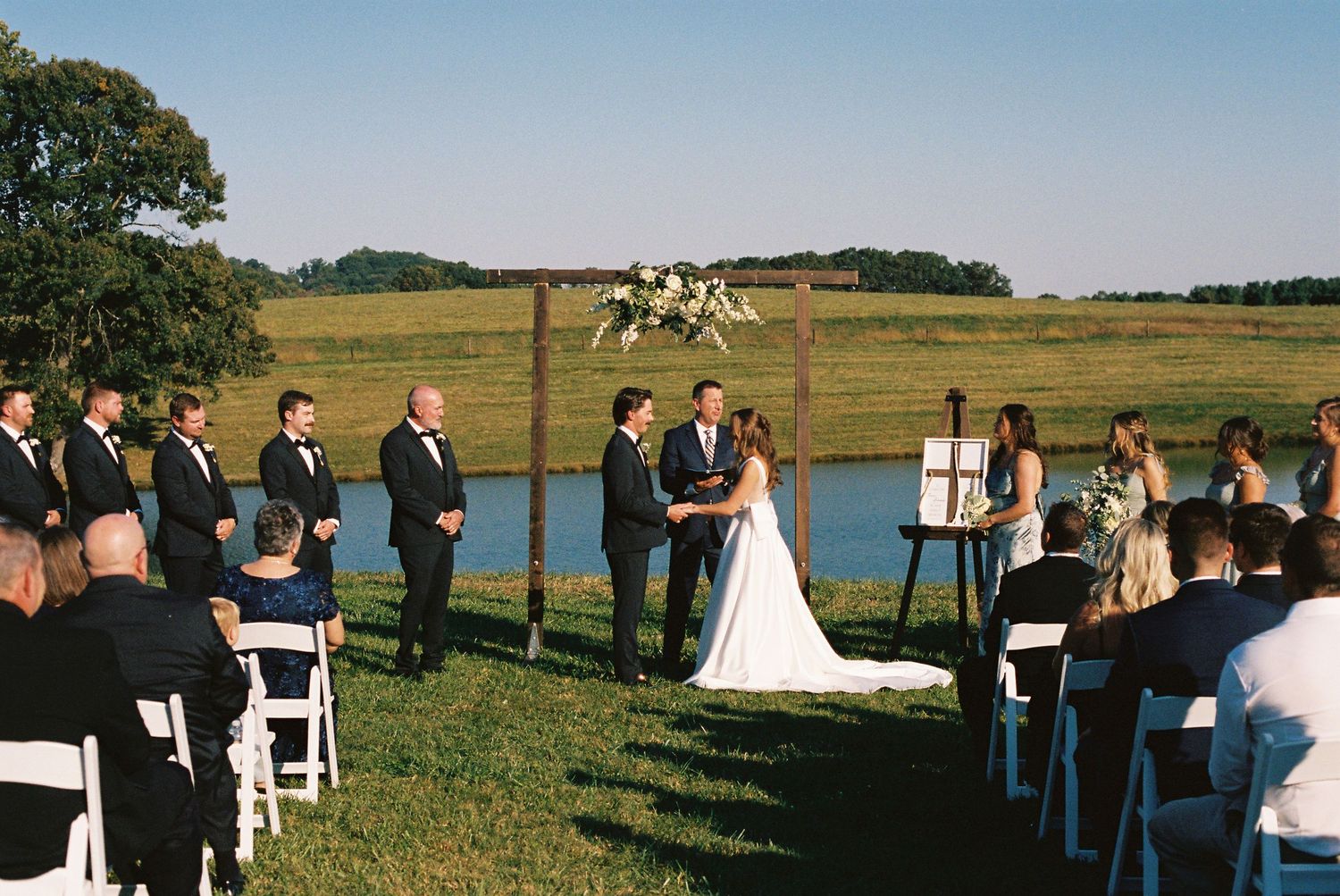 Panoramic view of outdoor wedding ceremony with guests seated by a lake.