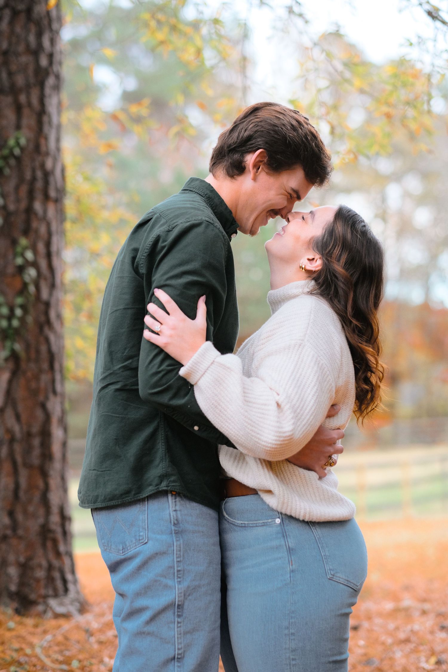 Couple embracing and laughing together on ground covered with orange autumn leaves.