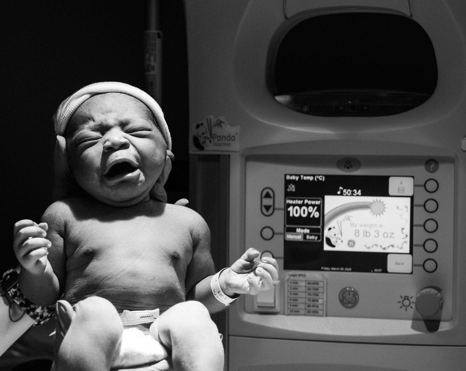 A newborn baby lies on a hospital bed under medical monitoring equipment.
