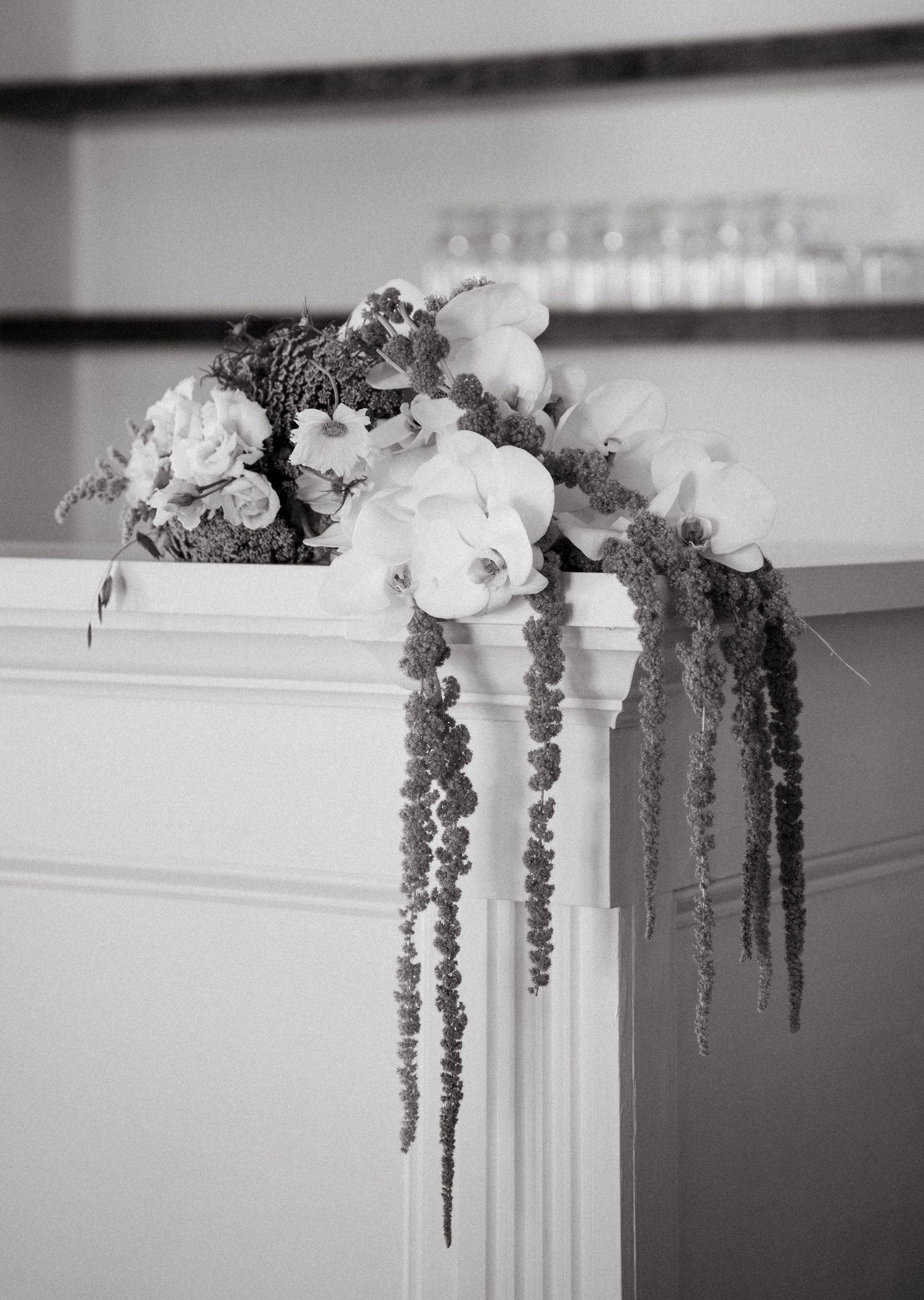 White floral and greenery arrangements cascade elegantly down decorative columns in a monochromatic black and white setting.