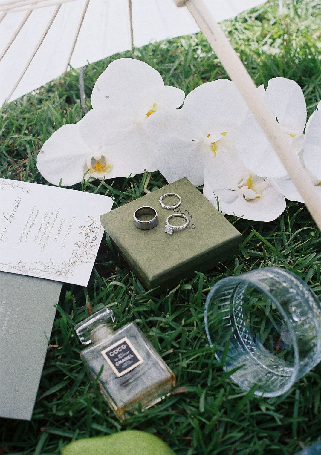 Wedding rings and white orchids displayed on a green surface with grass background.