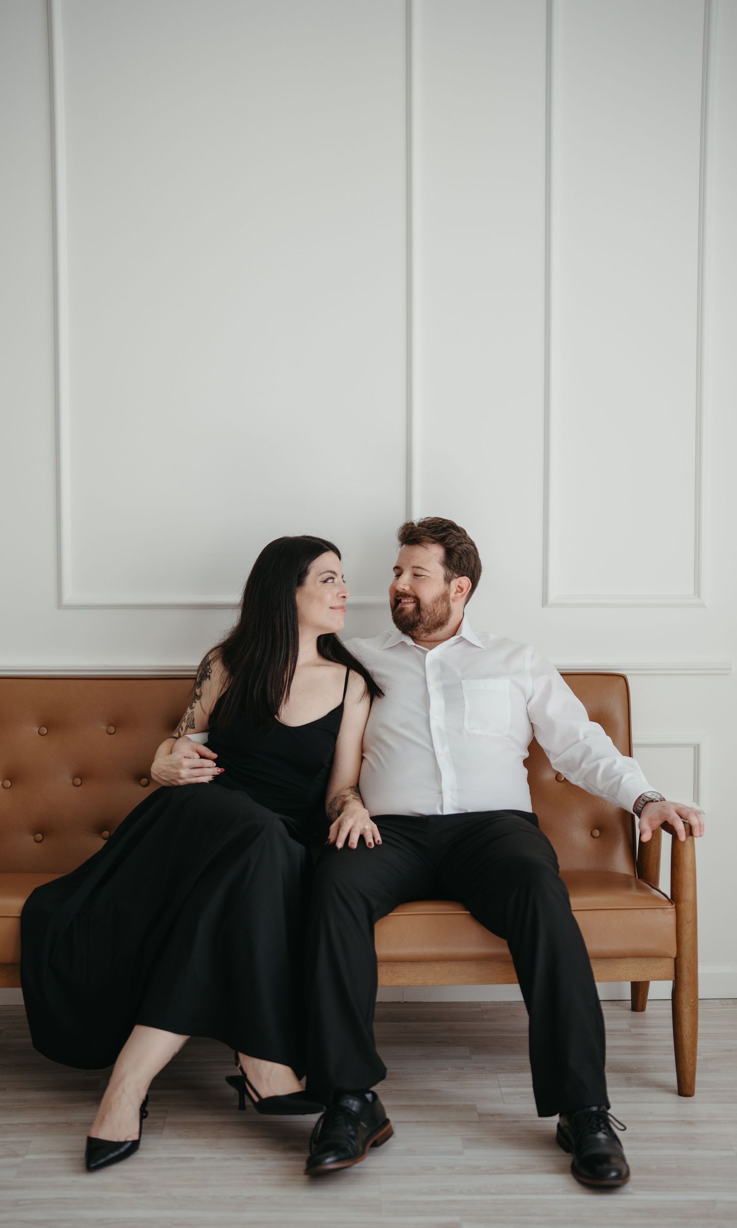 A couple in formal attire sharing an intimate moment on a leather couch.