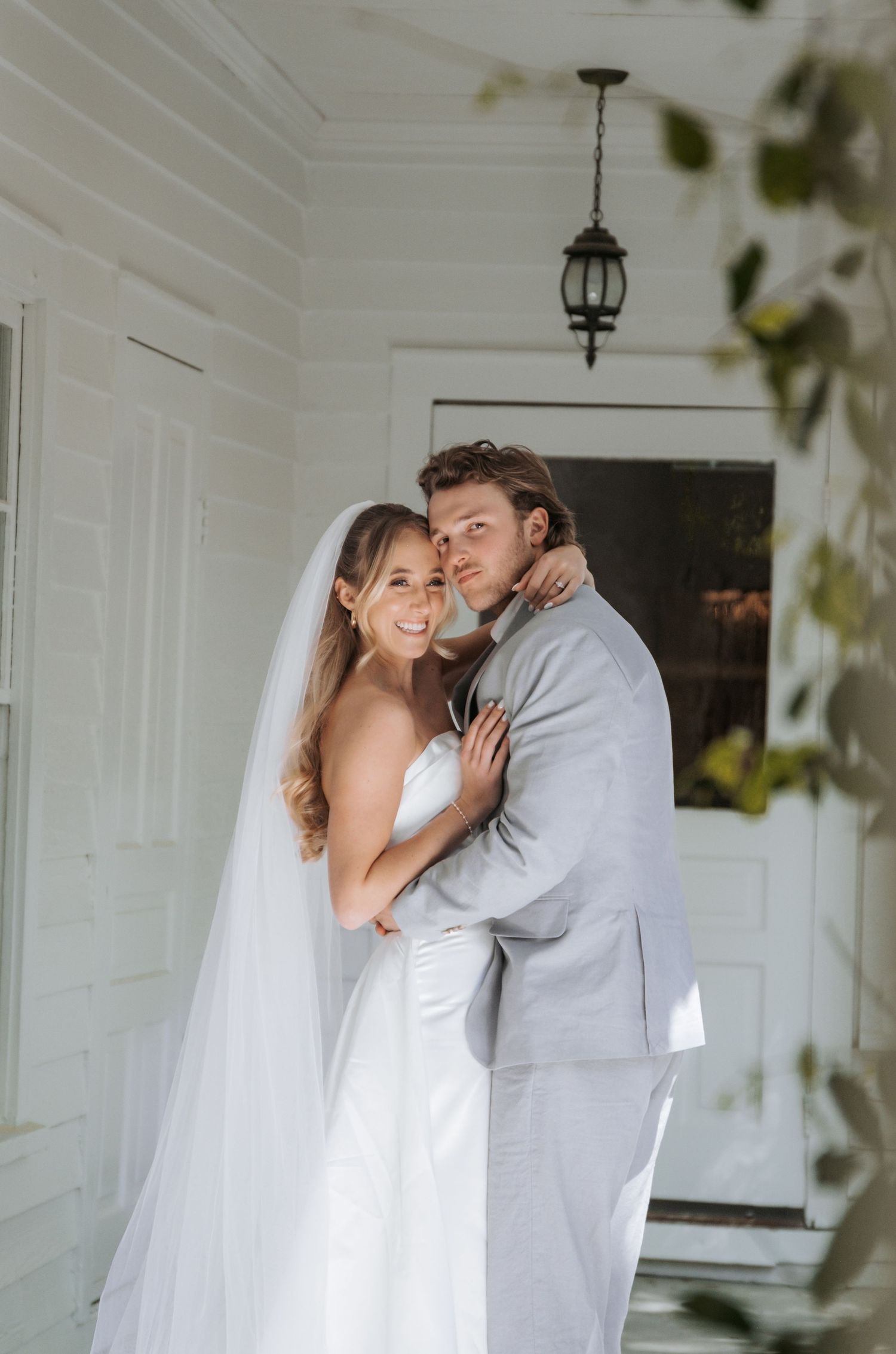 Newlywed couple embracing on white porch during intimate wedding moment.