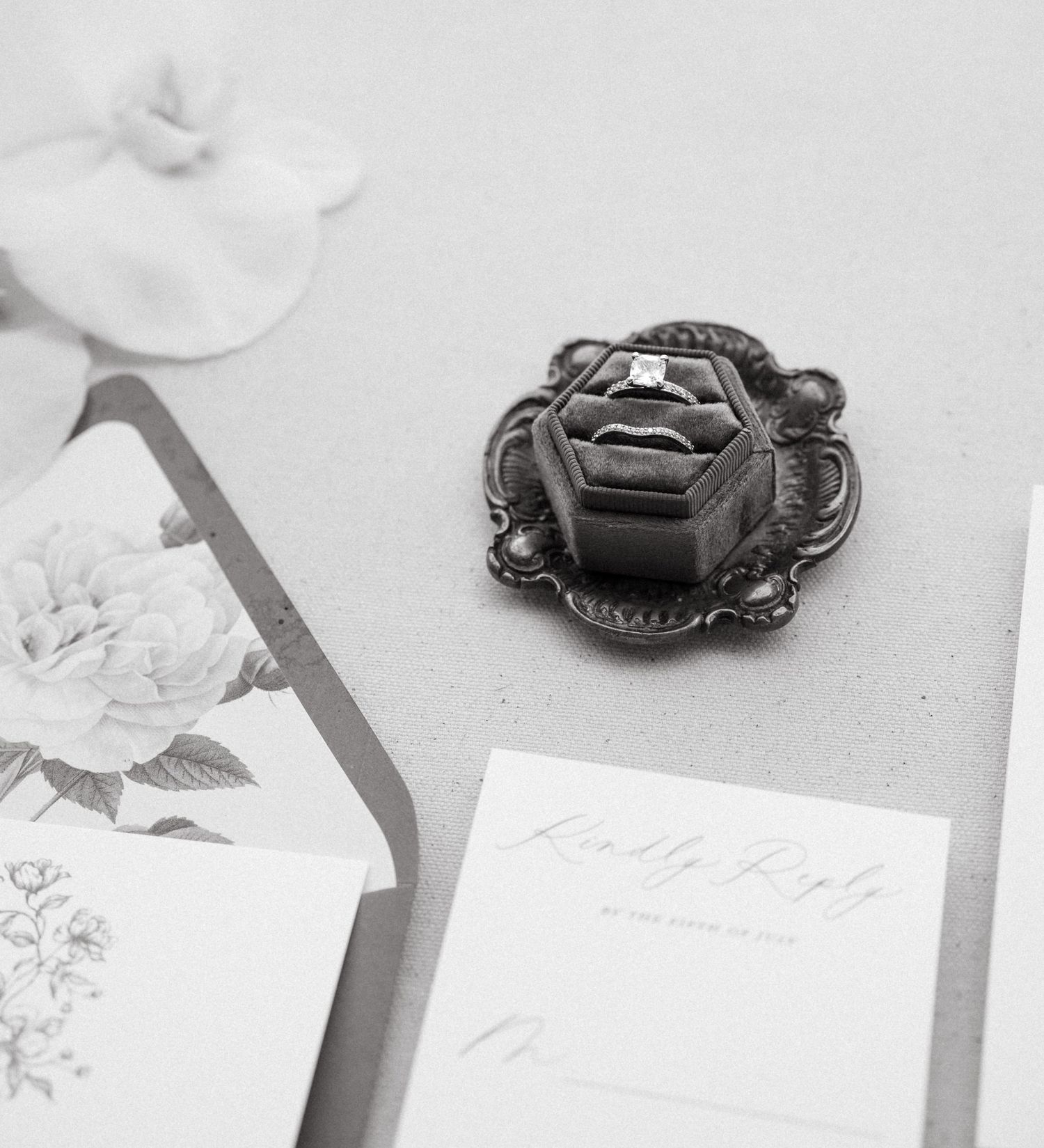 A vintage silver ring box sits on a table next to floral stationery and paper in an elegant black and white composition.