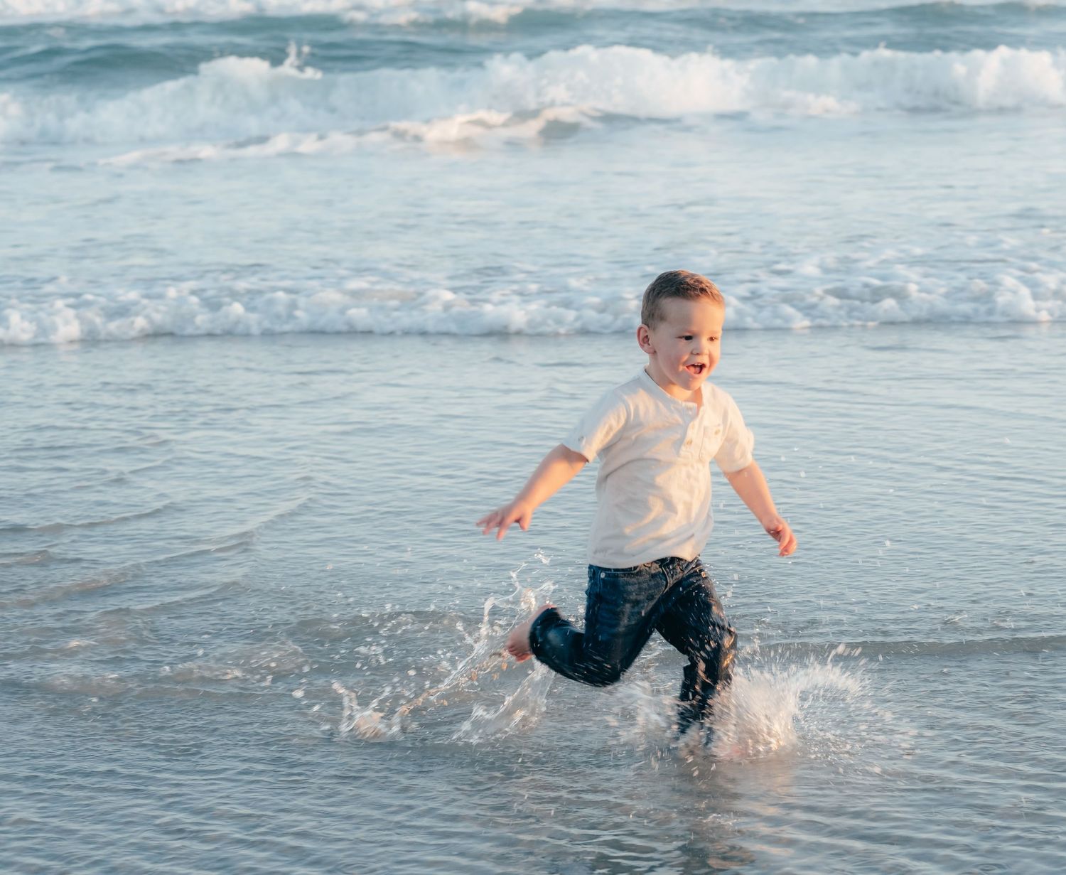Child playing and splashing in the ocean waves at sunset.