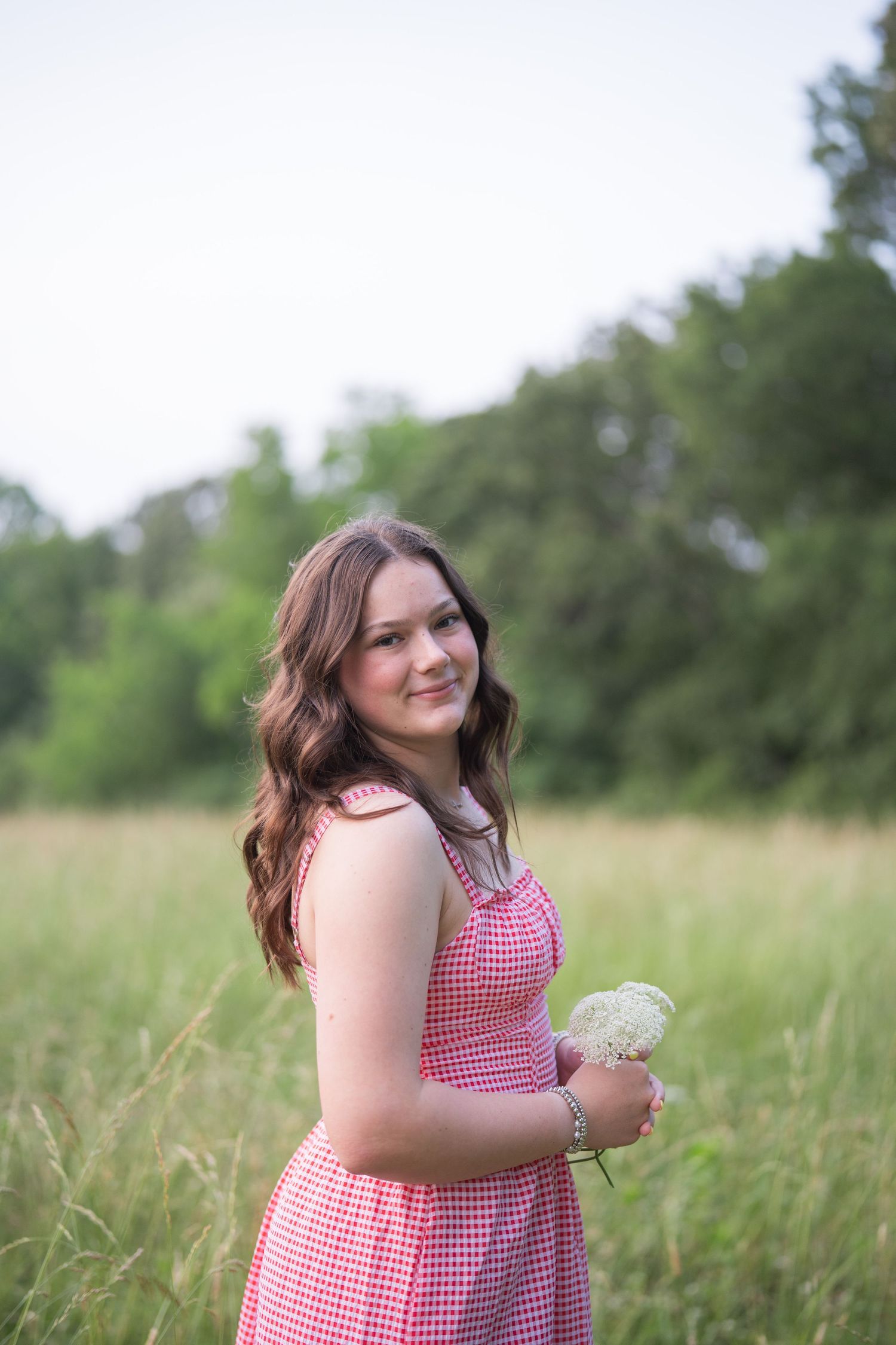 Woman in a pink gingham dress holding a delicate flower in a summer field.
