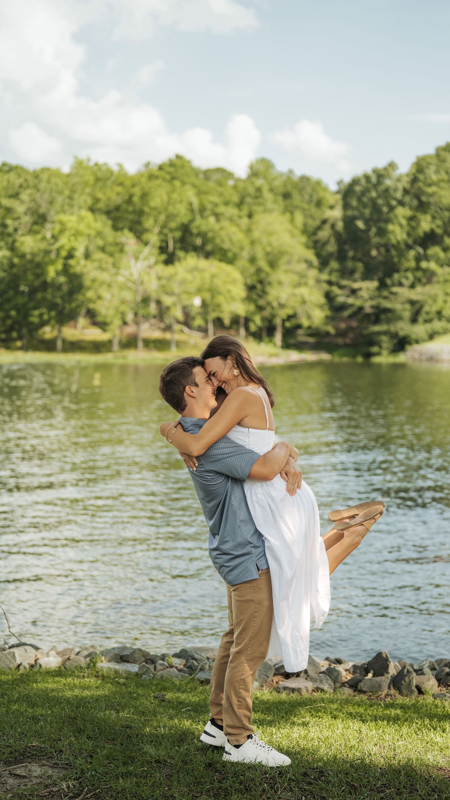 Couple celebrating engagement with joyful lifts and embraces by the water.