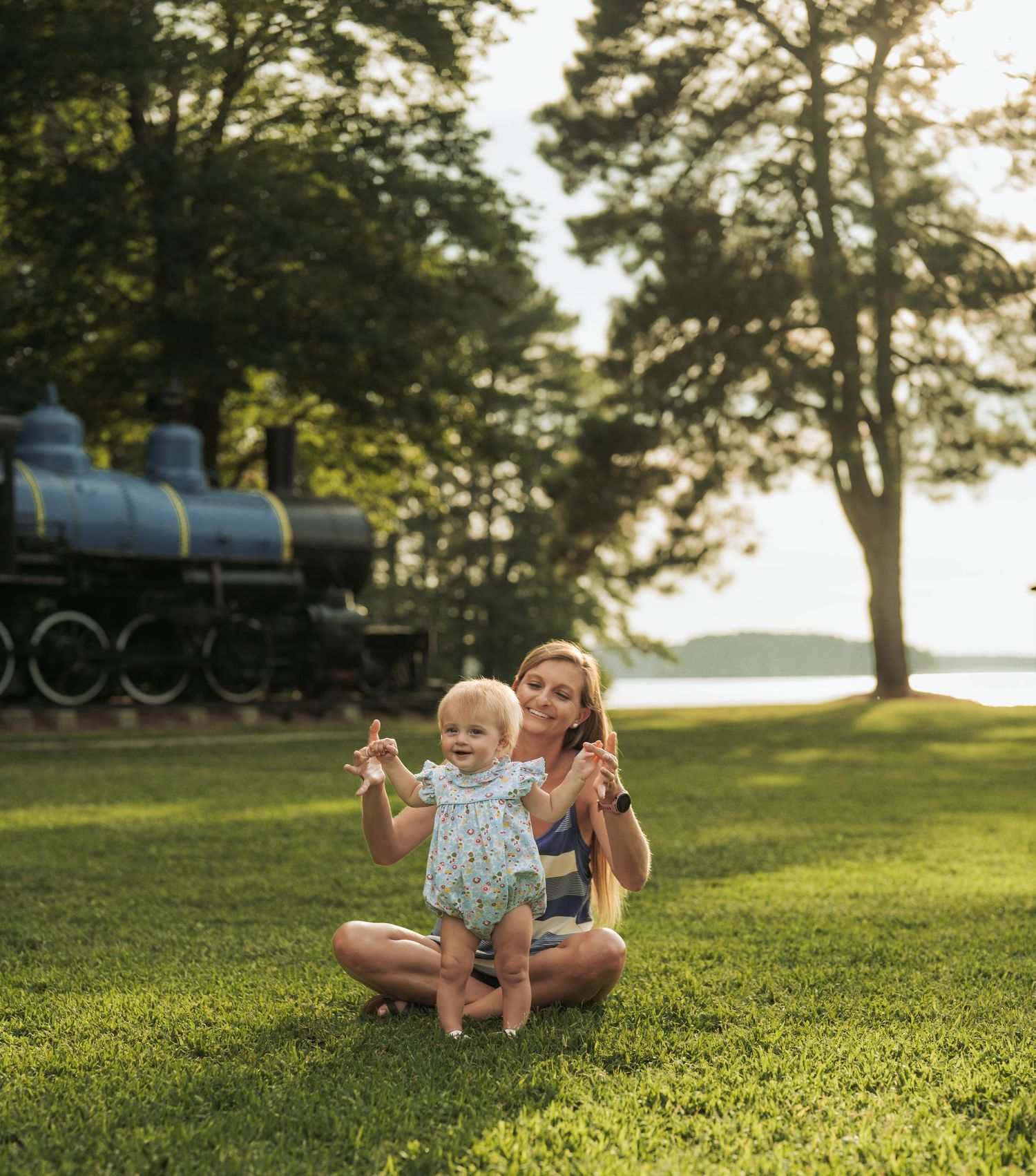 Family enjoying a summer evening on grassy hill with train and gazebo in background.