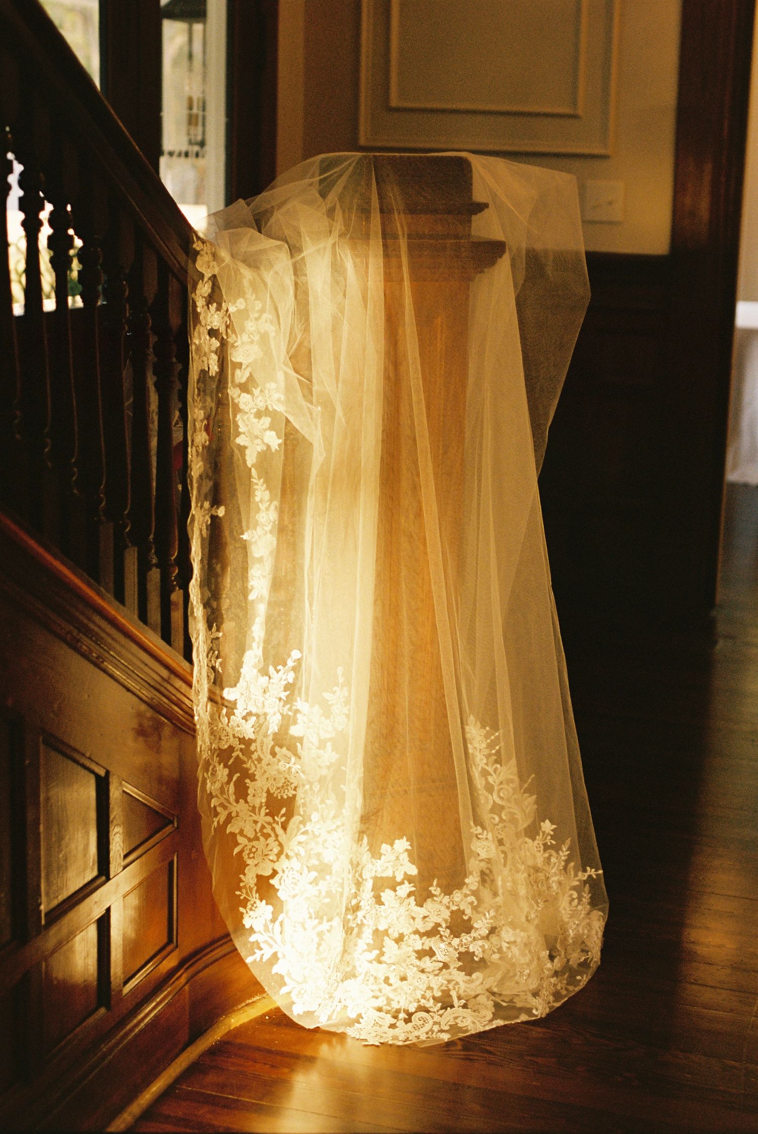 Ethereal wedding veil glowing with backlit illumination against dark wooden stairs.
