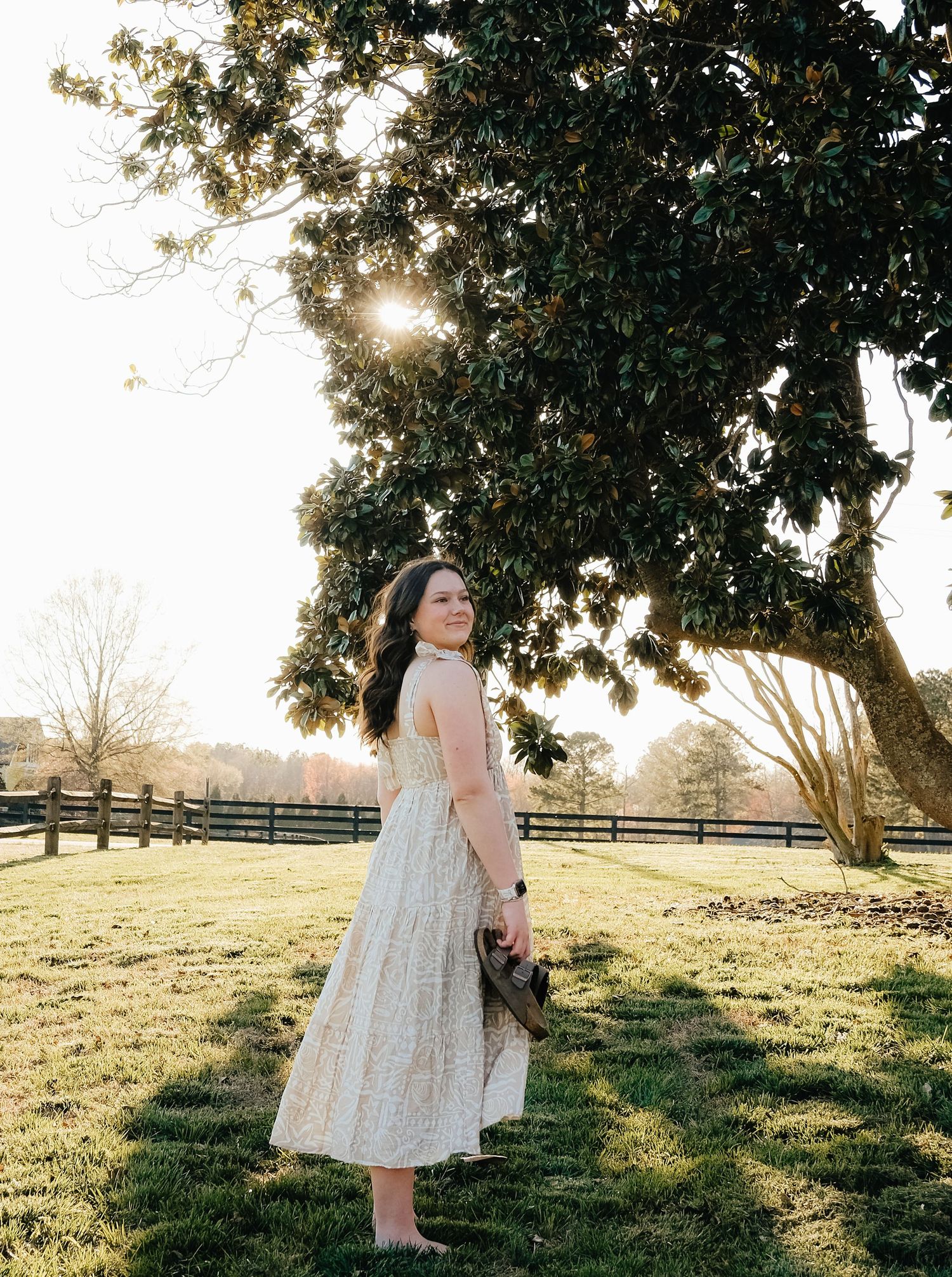 Sunlit outdoor portrait in a flowing dress against rustic fence and golden hour lighting.