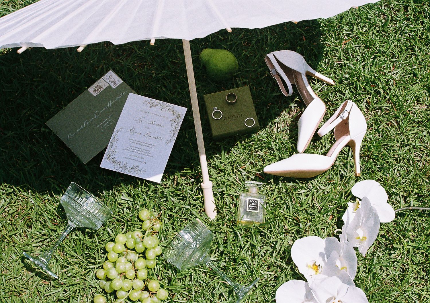 Wedding details including rings, orchids, and cards laid out on green lawn.