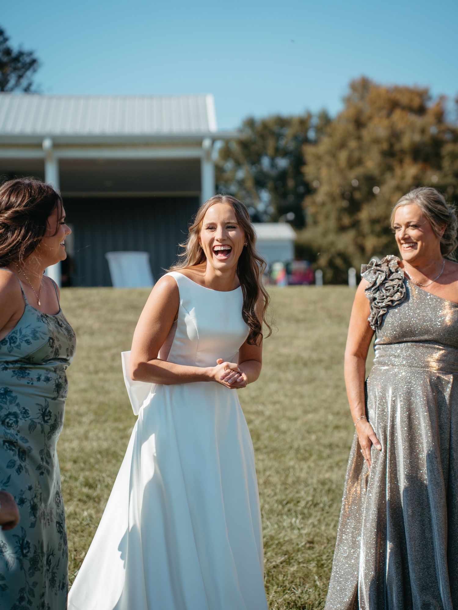 A group of people in formal attire laughing and interacting outdoors on a sunny day.