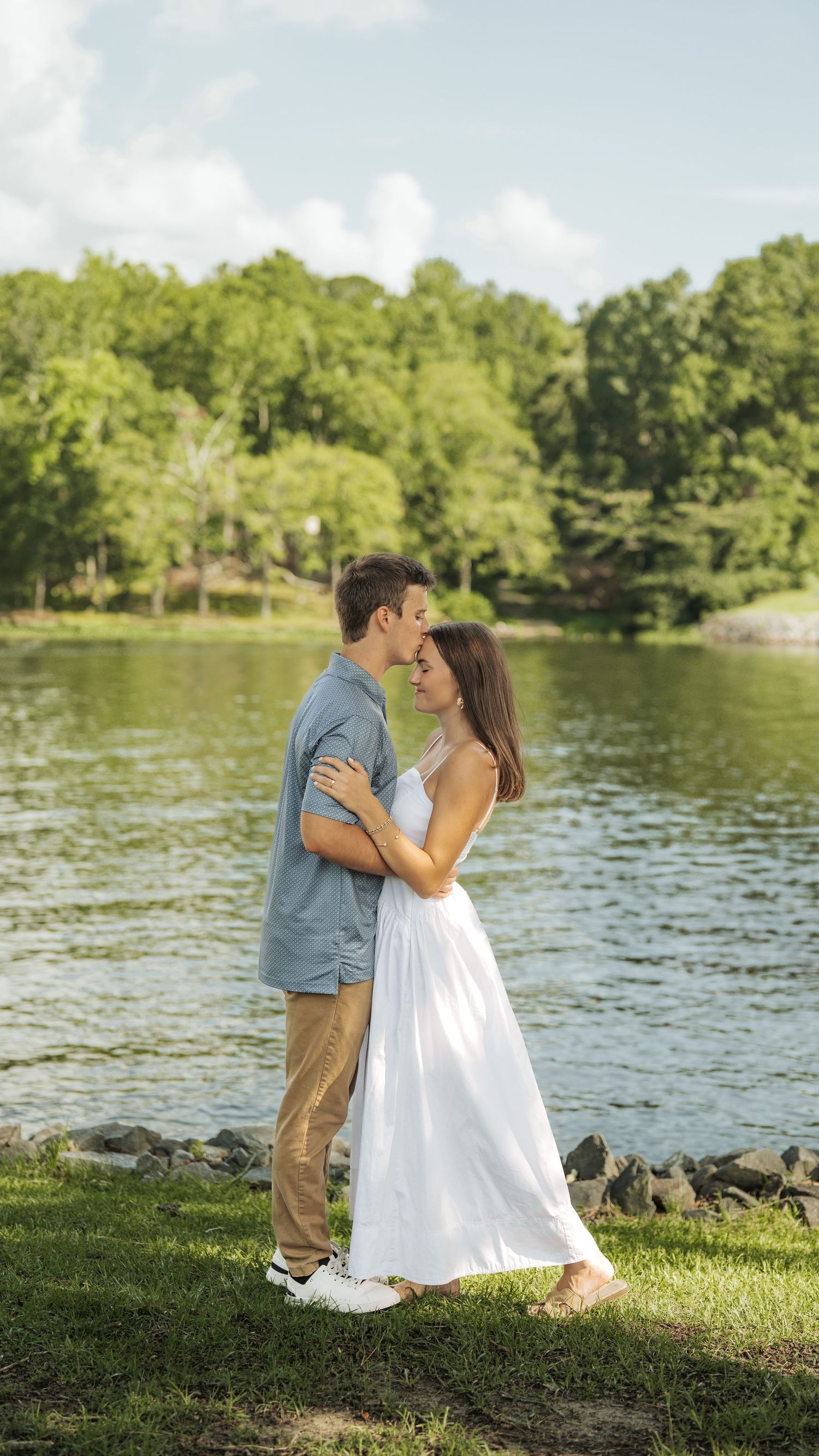 Couple in white dress and blue shirt sharing romantic moments by a lake.