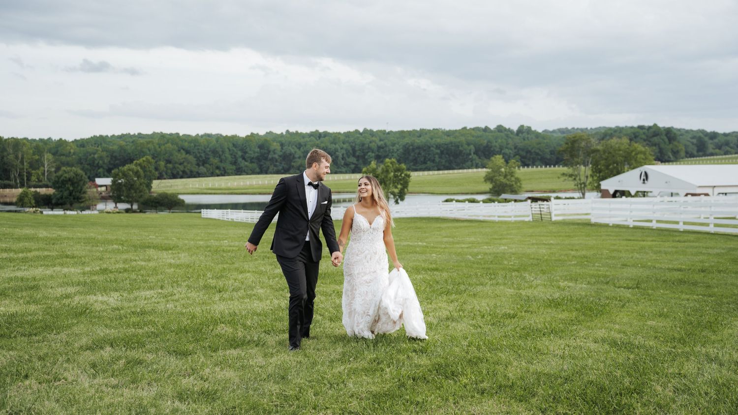 A couple walks together on a grassy lawn with a lake view in the background.