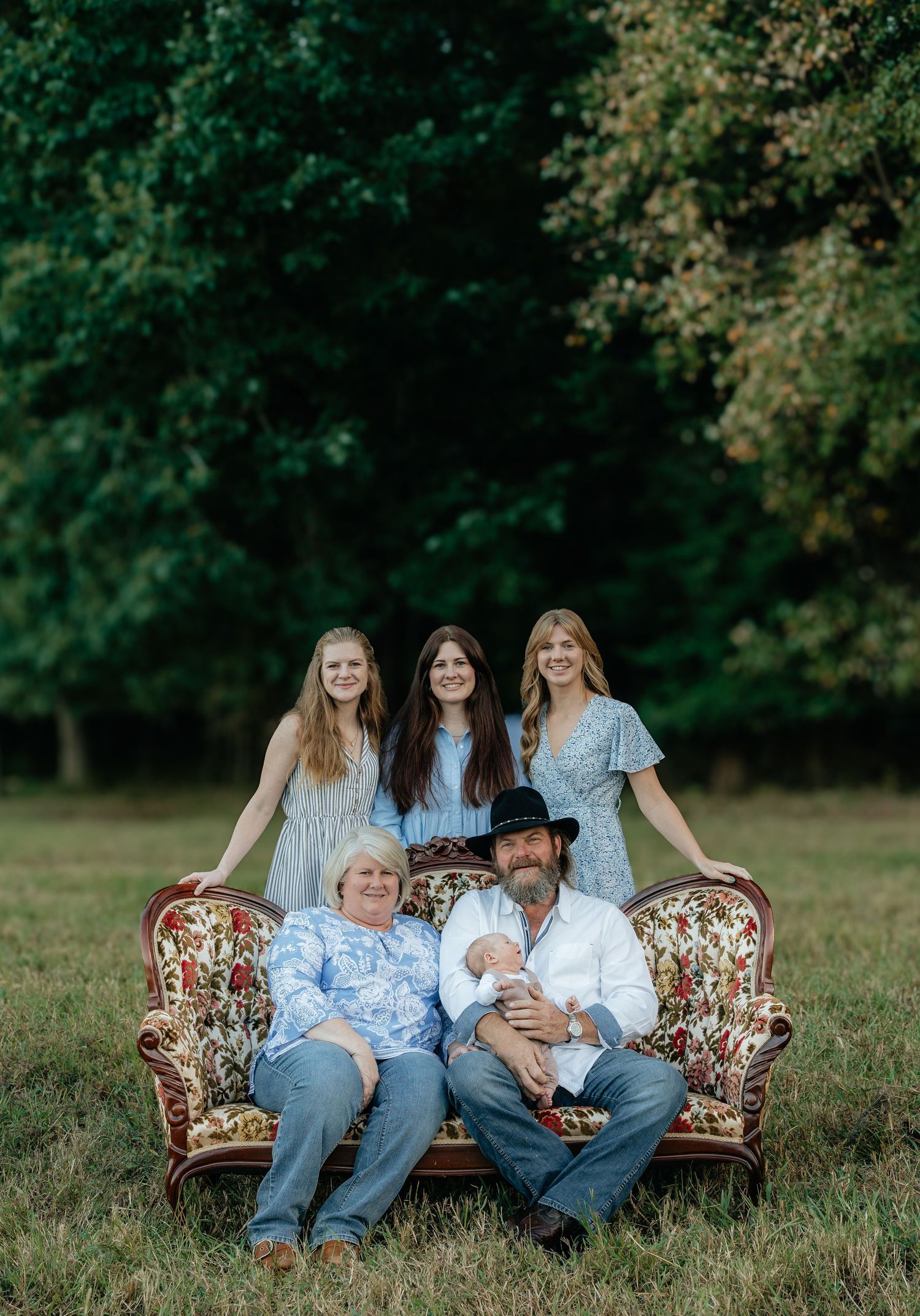 Family group seated on vintage floral couch in outdoor setting.