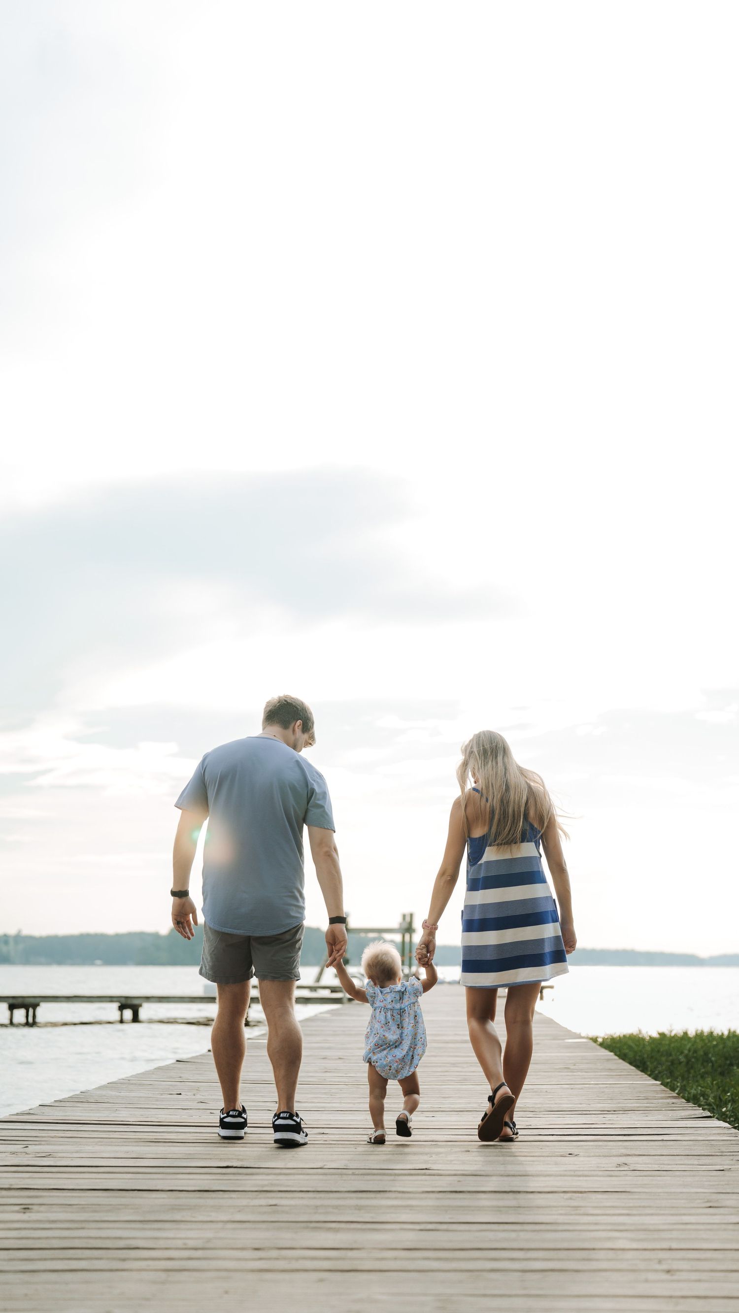 Family walking together on wooden boardwalk by the water at sunset.