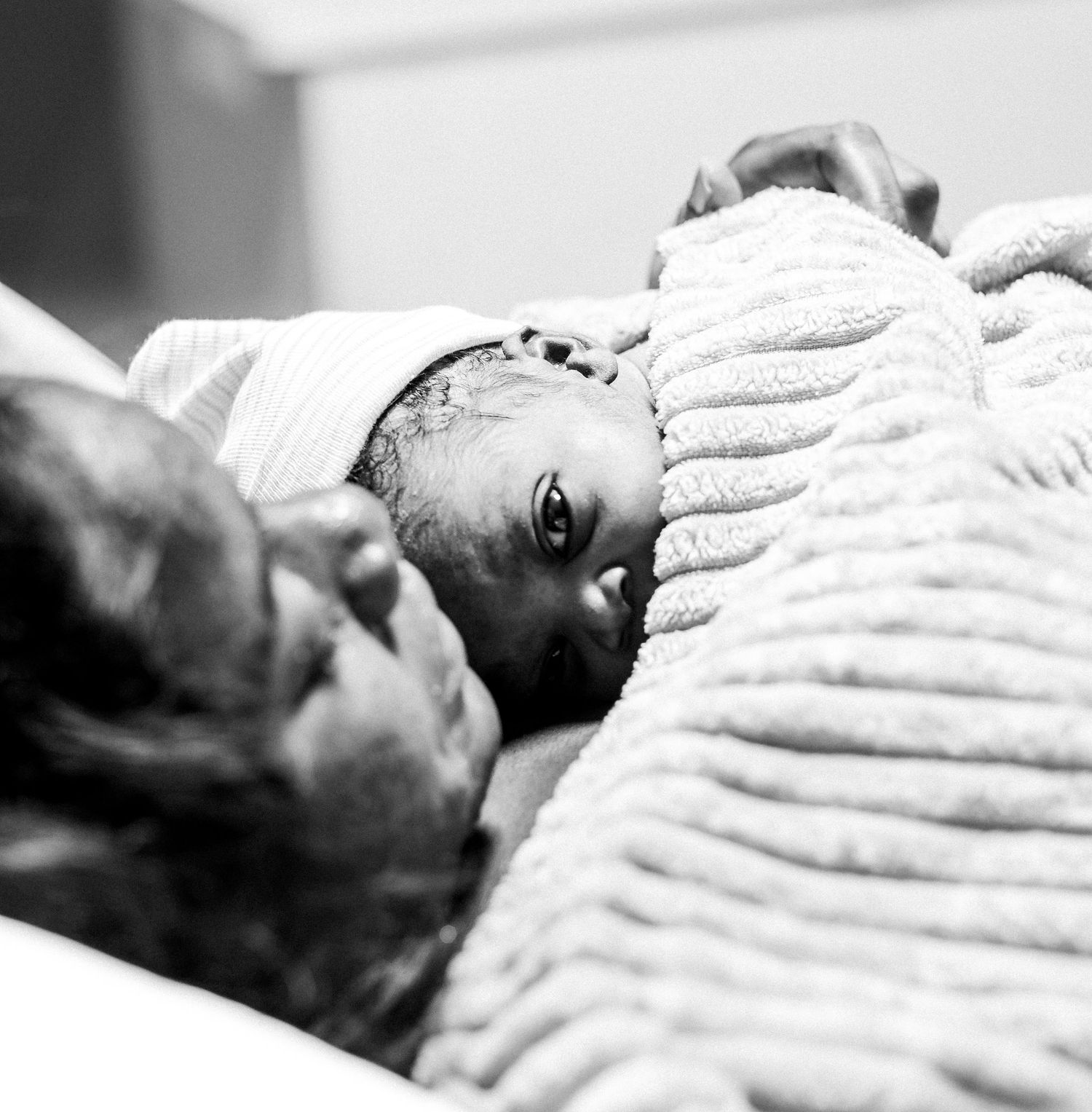 Intimate black and white portrait of a newborn baby resting on plush bedding.