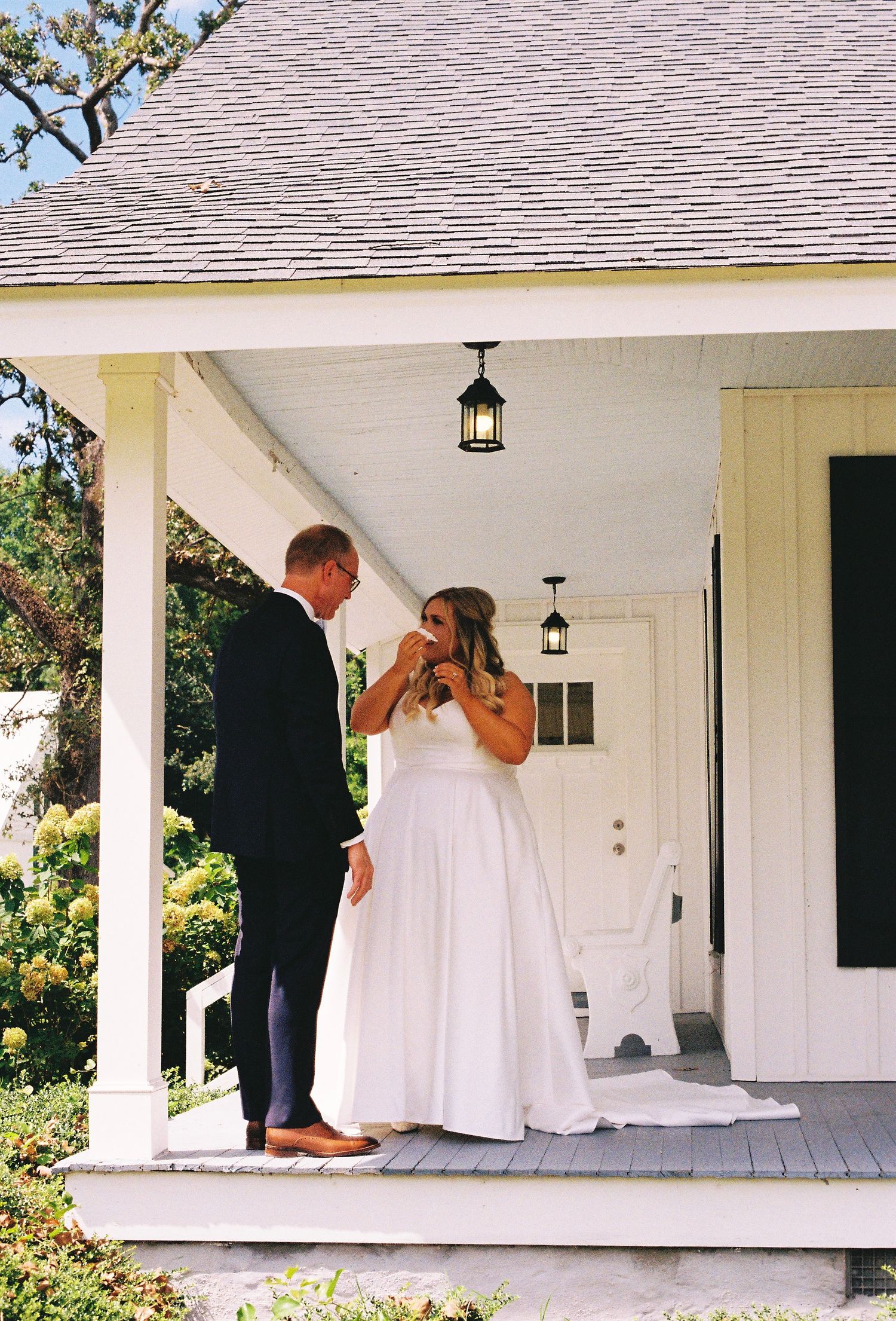 Wedding dress being arranged on a white porch with classic architectural details.