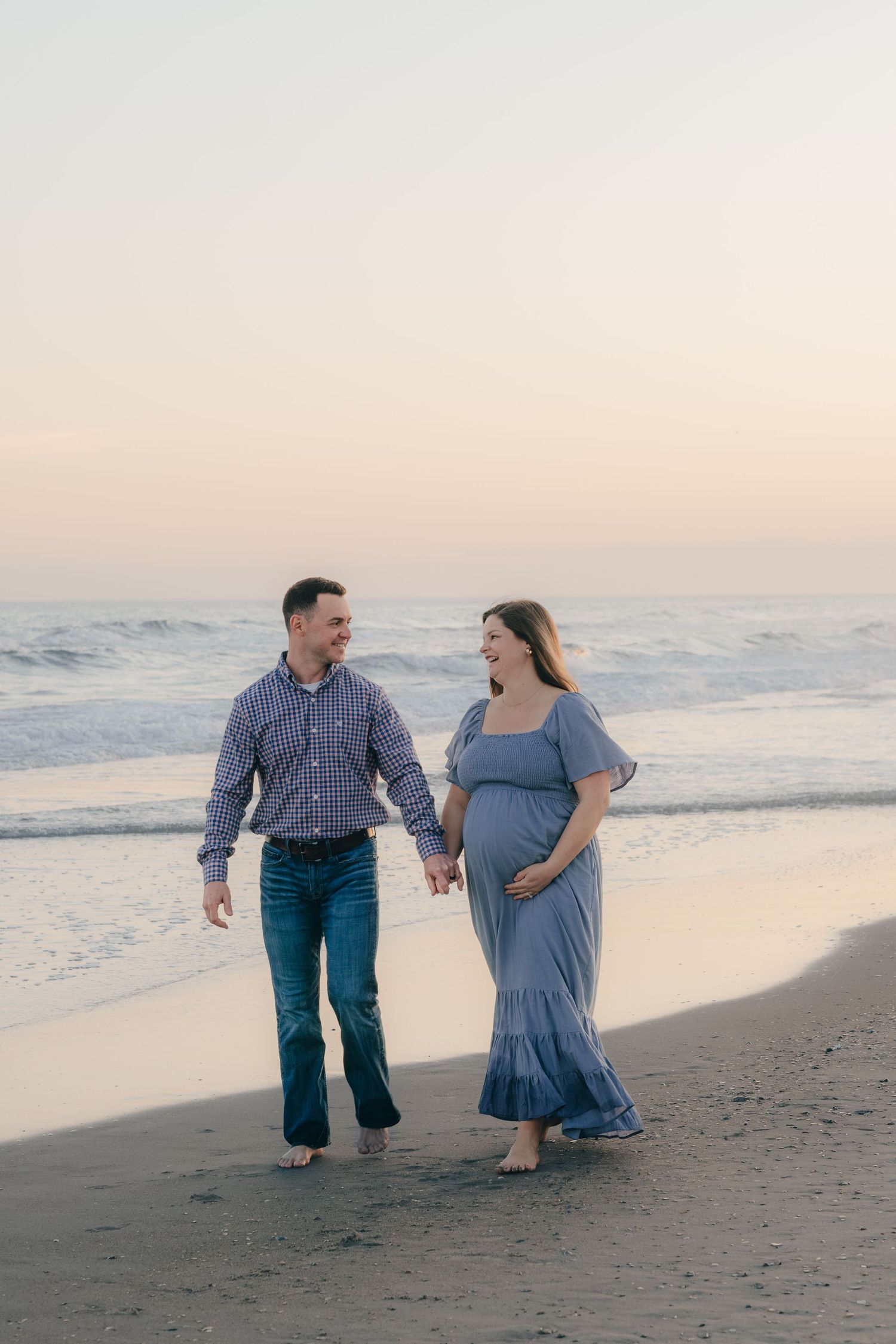 Couple walking together on beach at sunset with waves rolling in.