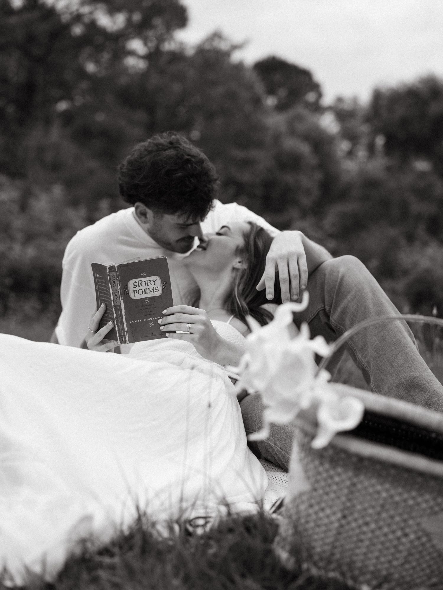 A couple shares intimate moments while lying on a picnic blanket in black and white.