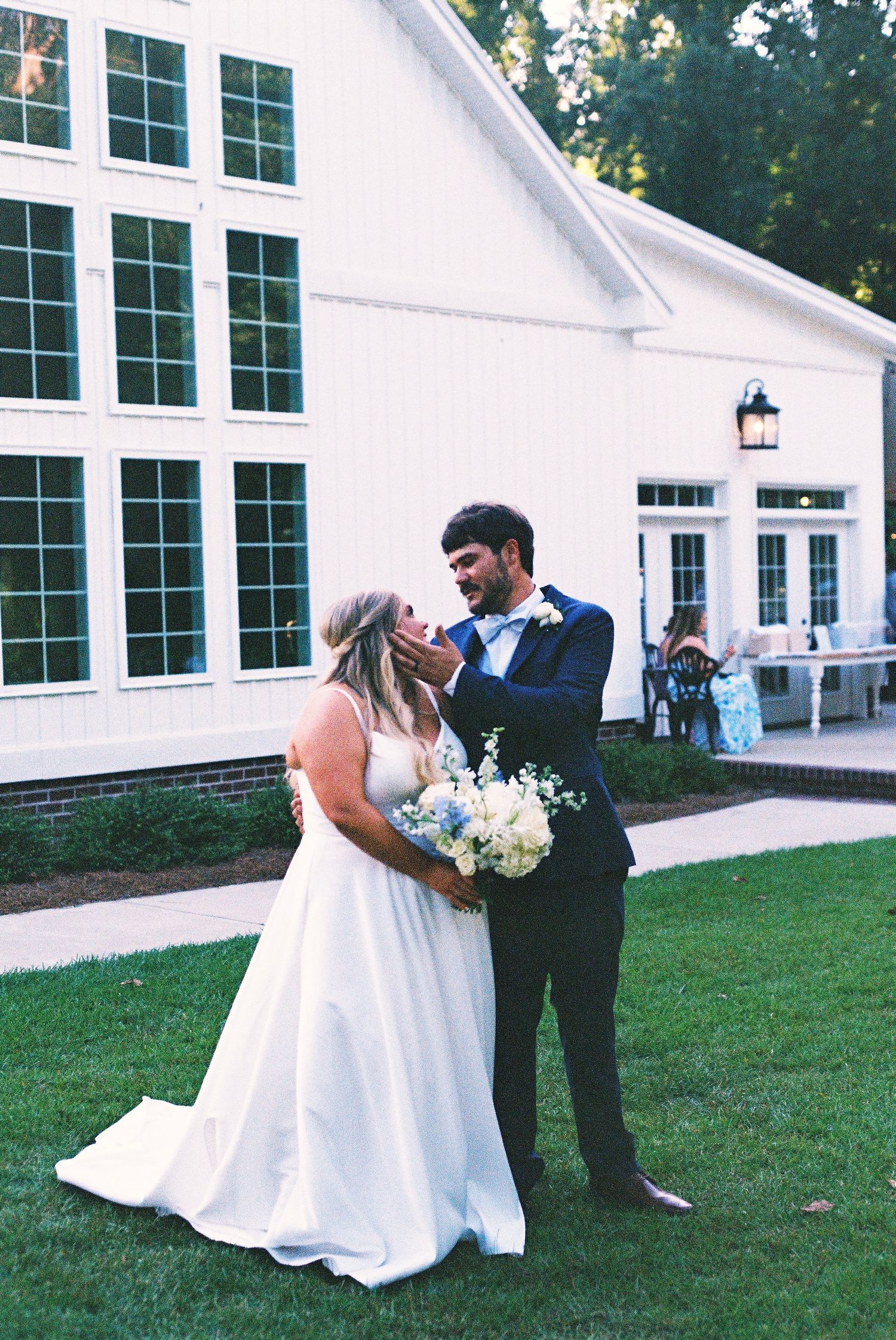Wedding couple embracing on the lawn outside a white chapel building.