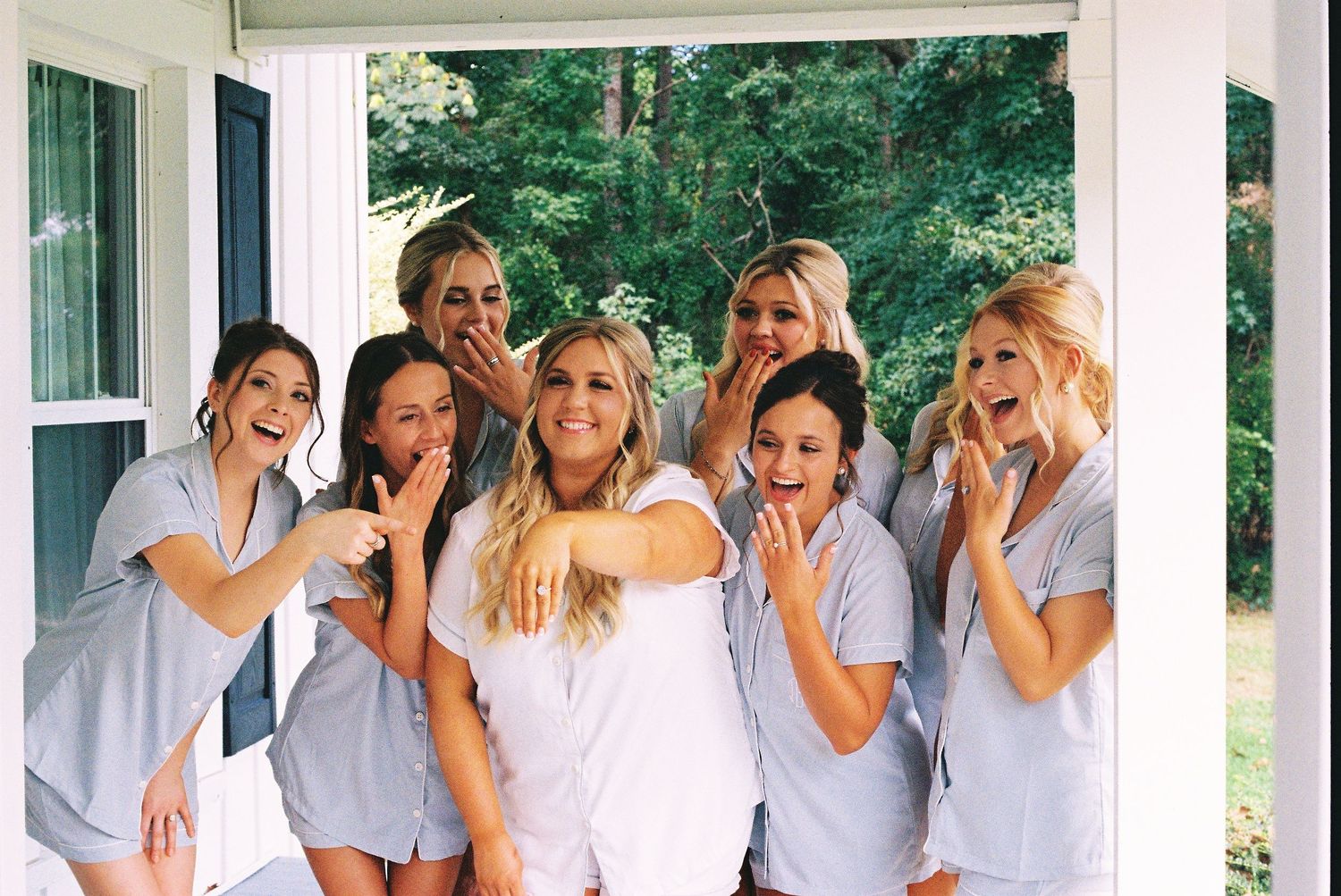 Group in matching light-colored outfits share a joyful moment on a white porch.