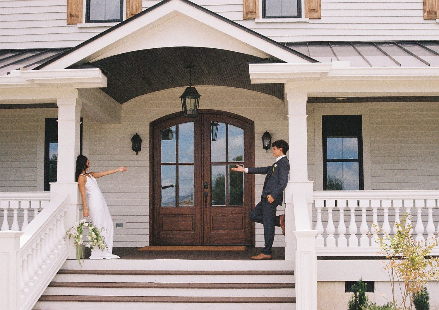 White farmhouse exterior with wooden shutters and wraparound porch features classic architectural details.