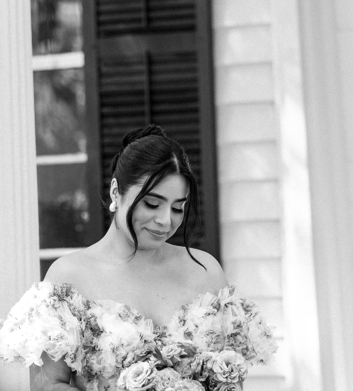 A person in a floral dress holds a bouquet while posing on a white columned porch.