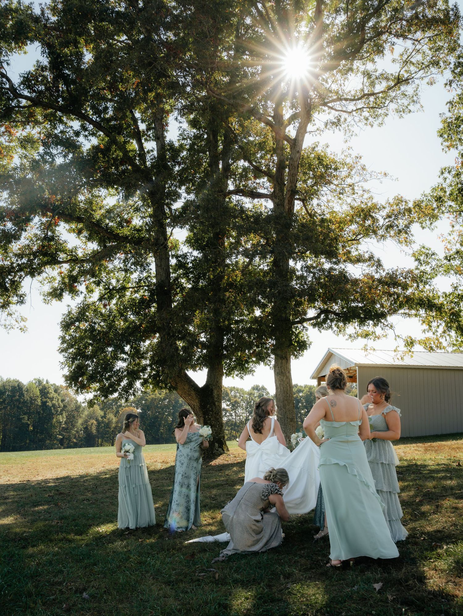 Wedding party relaxes on a grassy hillside during golden hour.