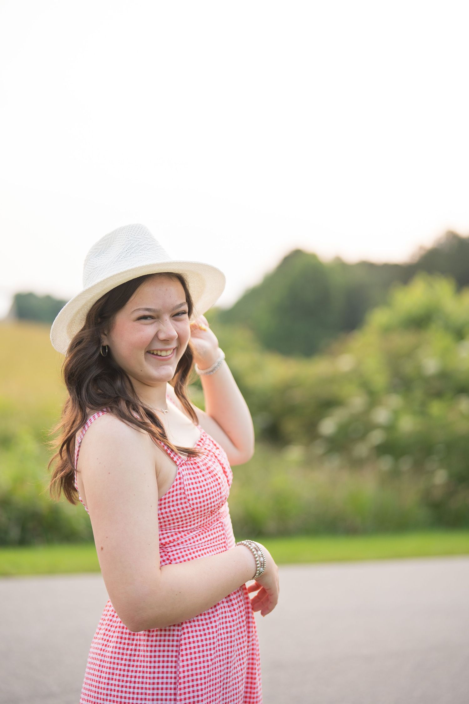 Person in a red gingham dress and sun hat enjoying a summer day in a field.