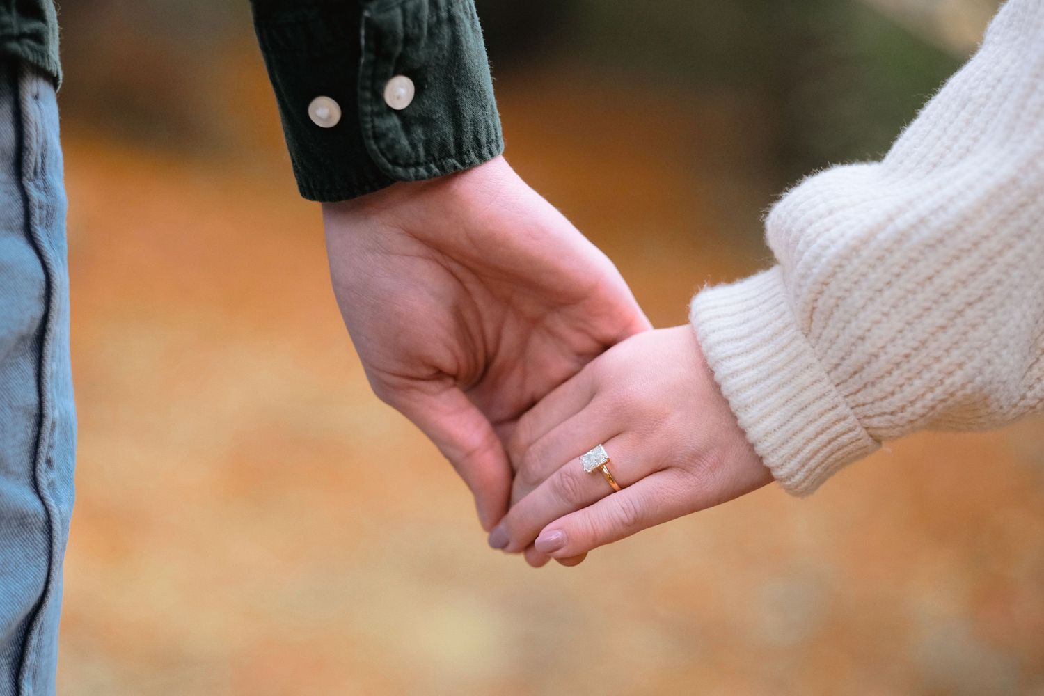 Close-up shot of couple holding hands against autumn ground.
