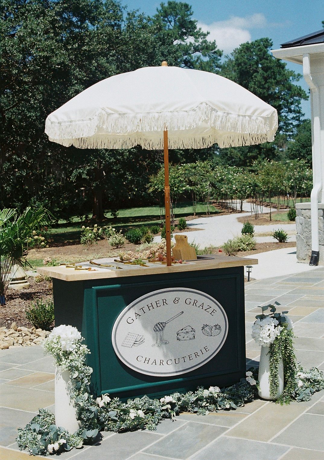 Elegant outdoor catering setup with white umbrellas and floral arrangements.