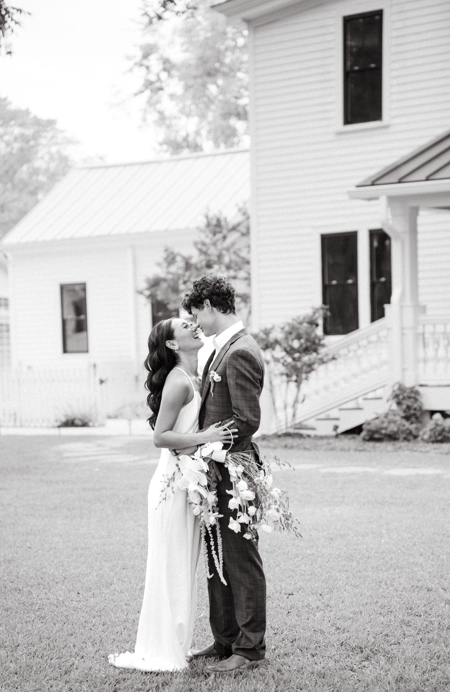 A romantic black and white wedding photo sequence showing a couple sharing a kiss on a lawn outside a white house.