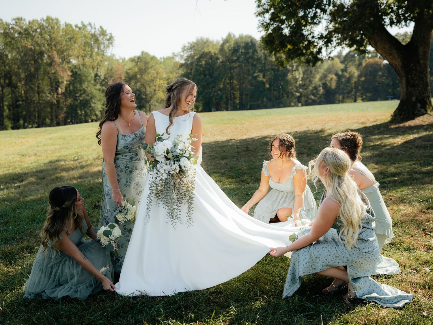 A group in formal attire sits together on grassy hillside during golden hour in a scenic outdoor setting.
