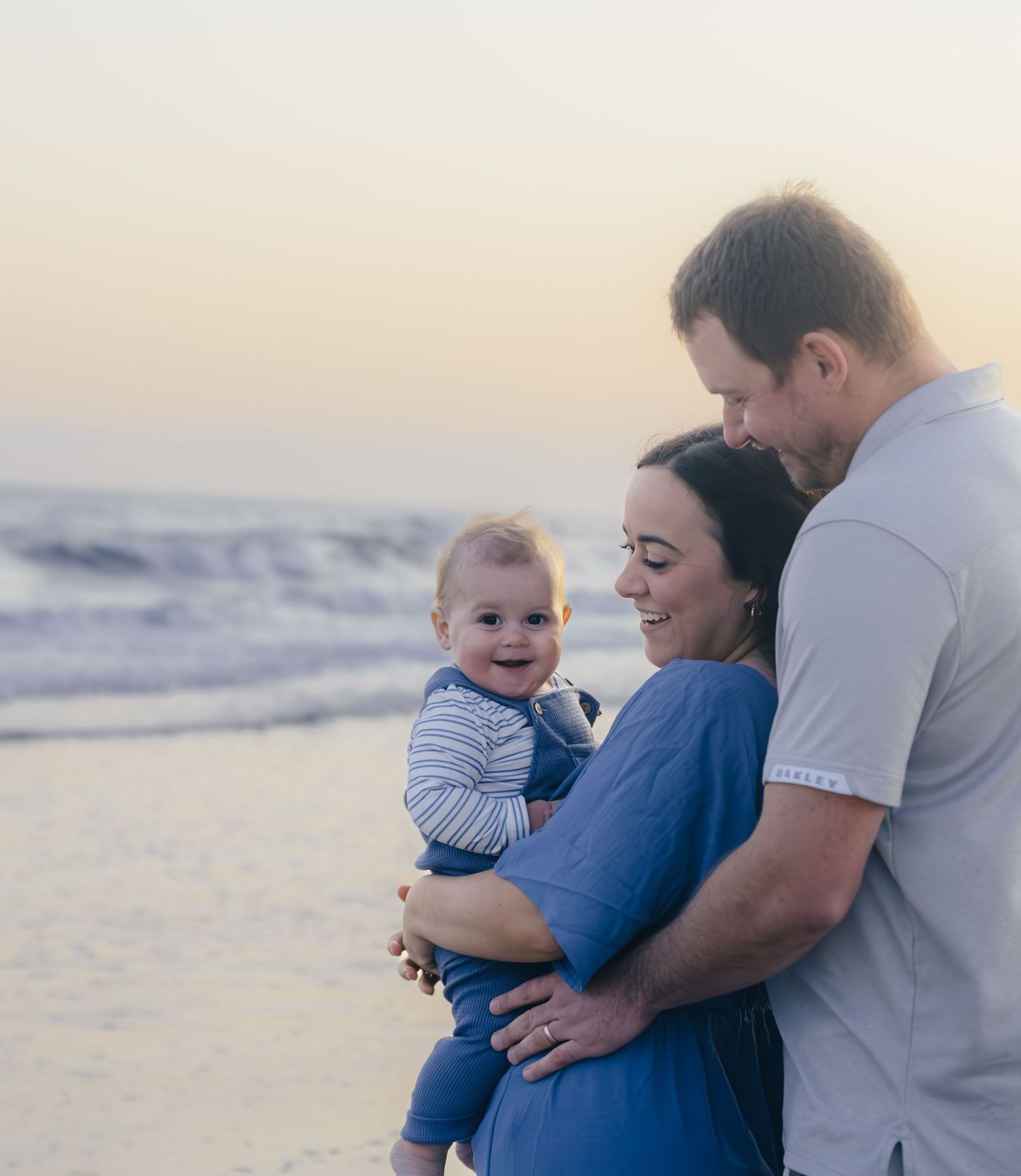 Family of three embracing on sandy beach during golden hour.