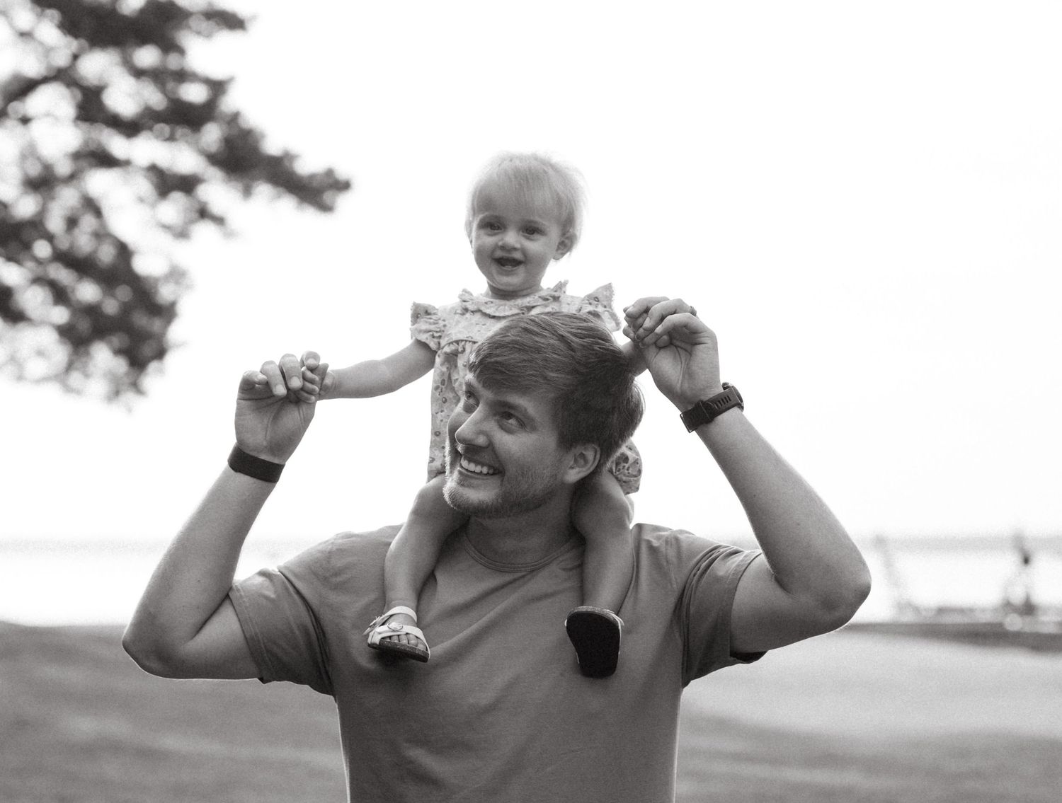 Black and white photo of playful shoulder rides in an outdoor park setting.