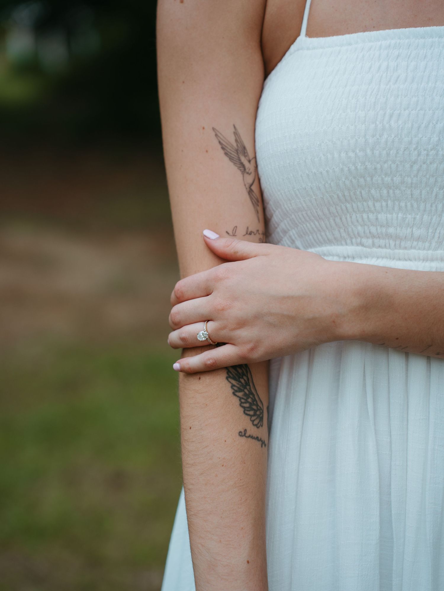 Close-up view of a person's arm with delicate tattoo artwork visible against a white dress background.