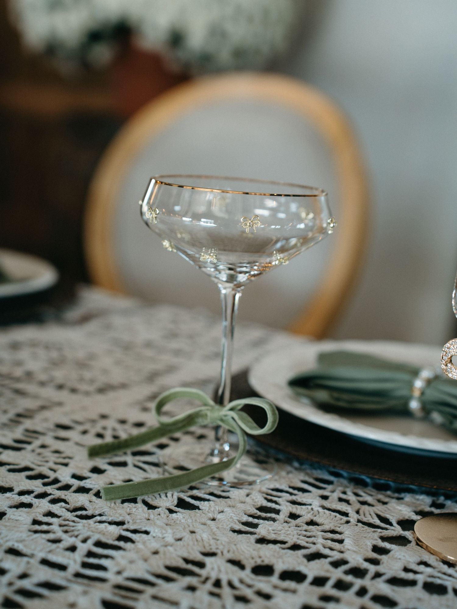 Crystal champagne coupe glasses sit on a white lace tablecloth in an elegant table setting.