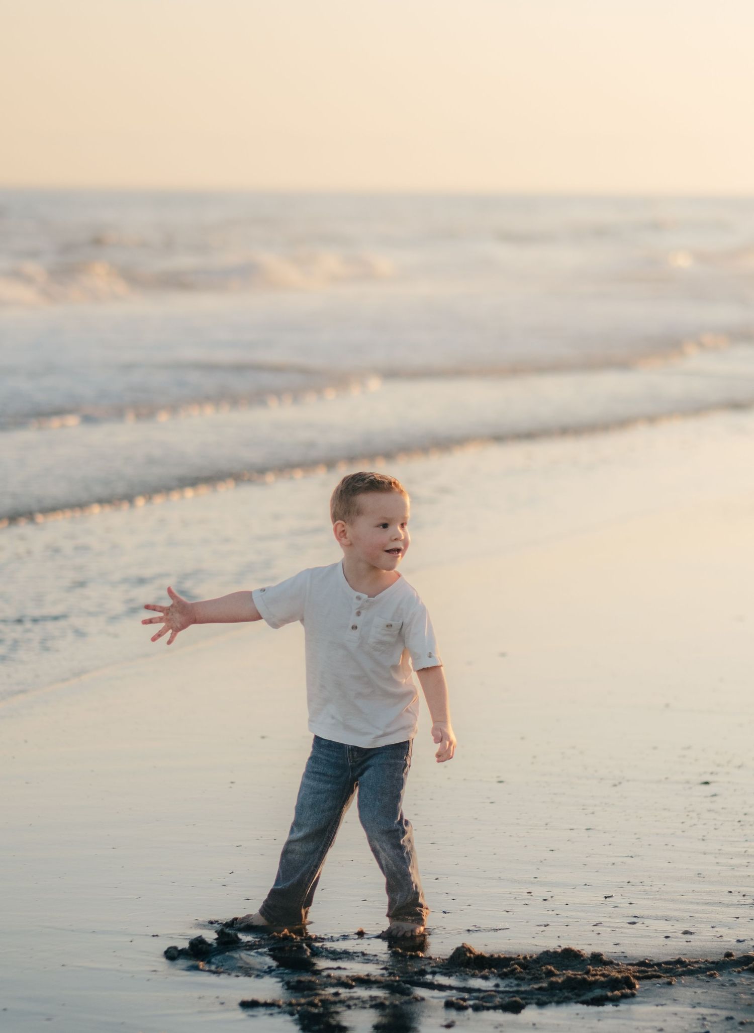 Young child splashing and playing in shallow ocean water at sunset.