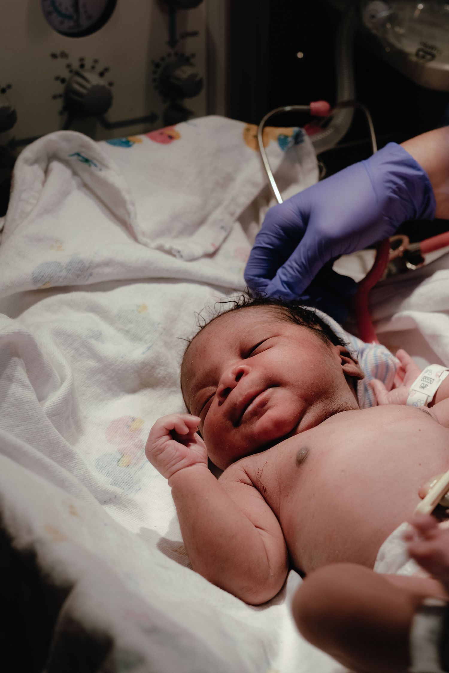Newborn baby resting on white blanket during medical examination.