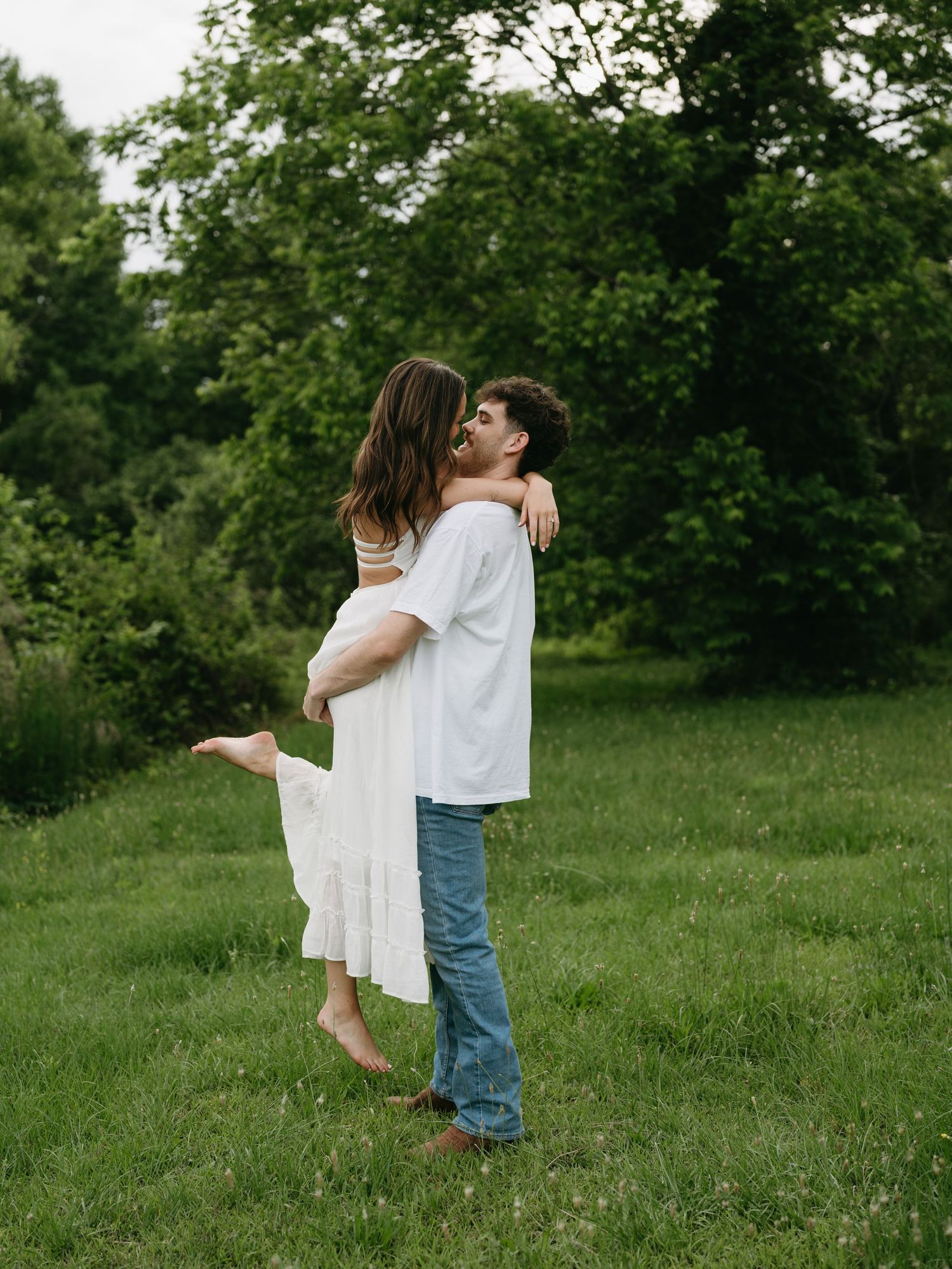 A romantic embrace in a lush green field with the woman's white dress flowing in the breeze.