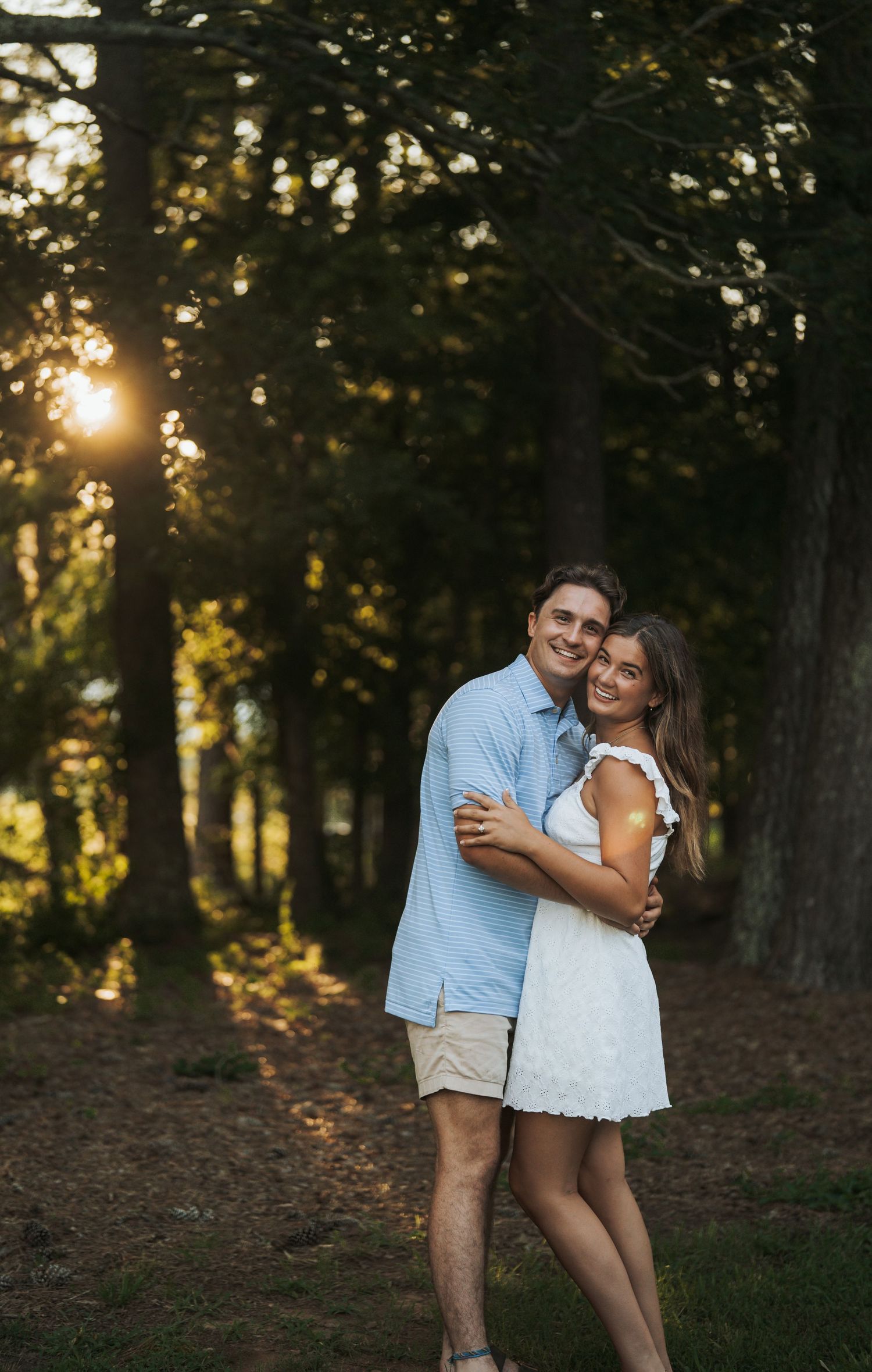 Romantic couple embracing in a wooded area during golden hour sunset.