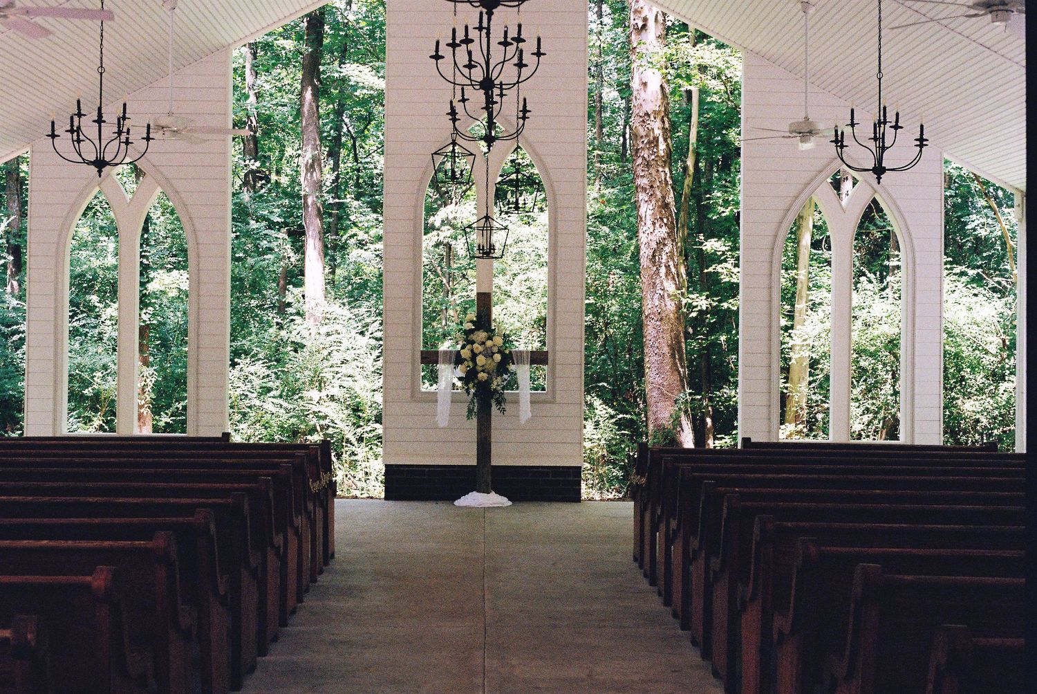 Elegant white chapel interior with chandeliers and wooden pews lined up for a wedding ceremony.