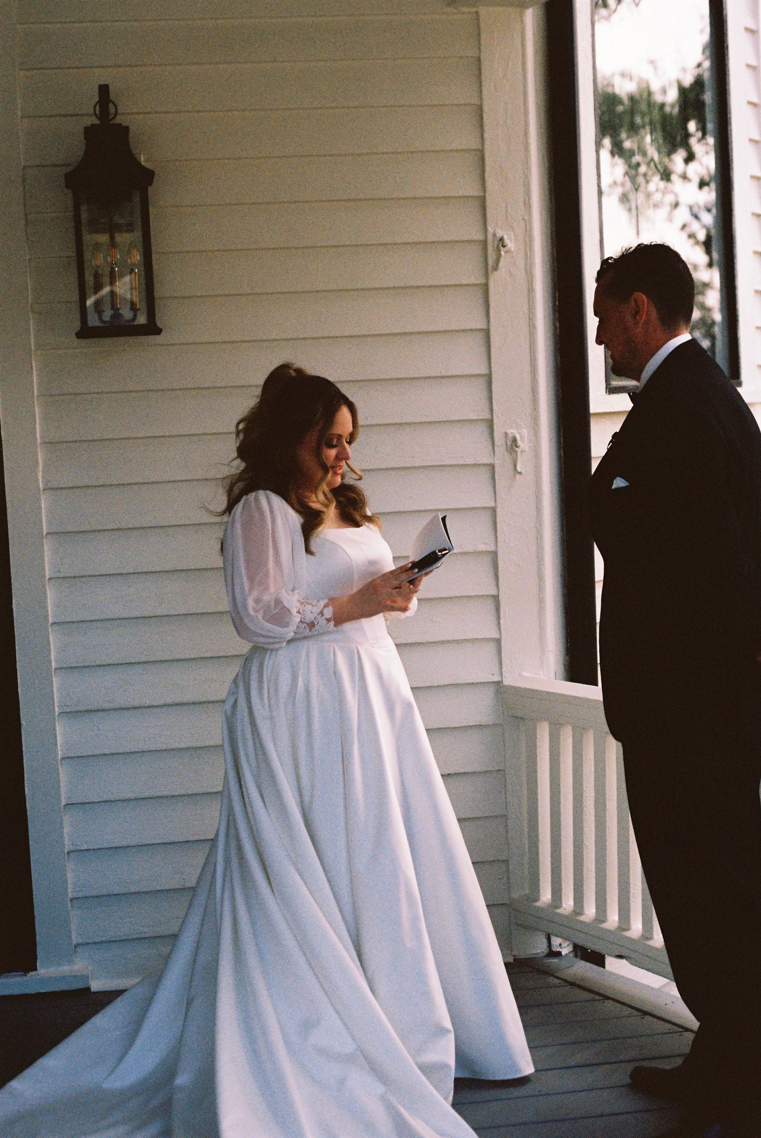 A wedding couple shares moments on a white farmhouse porch captured on film.