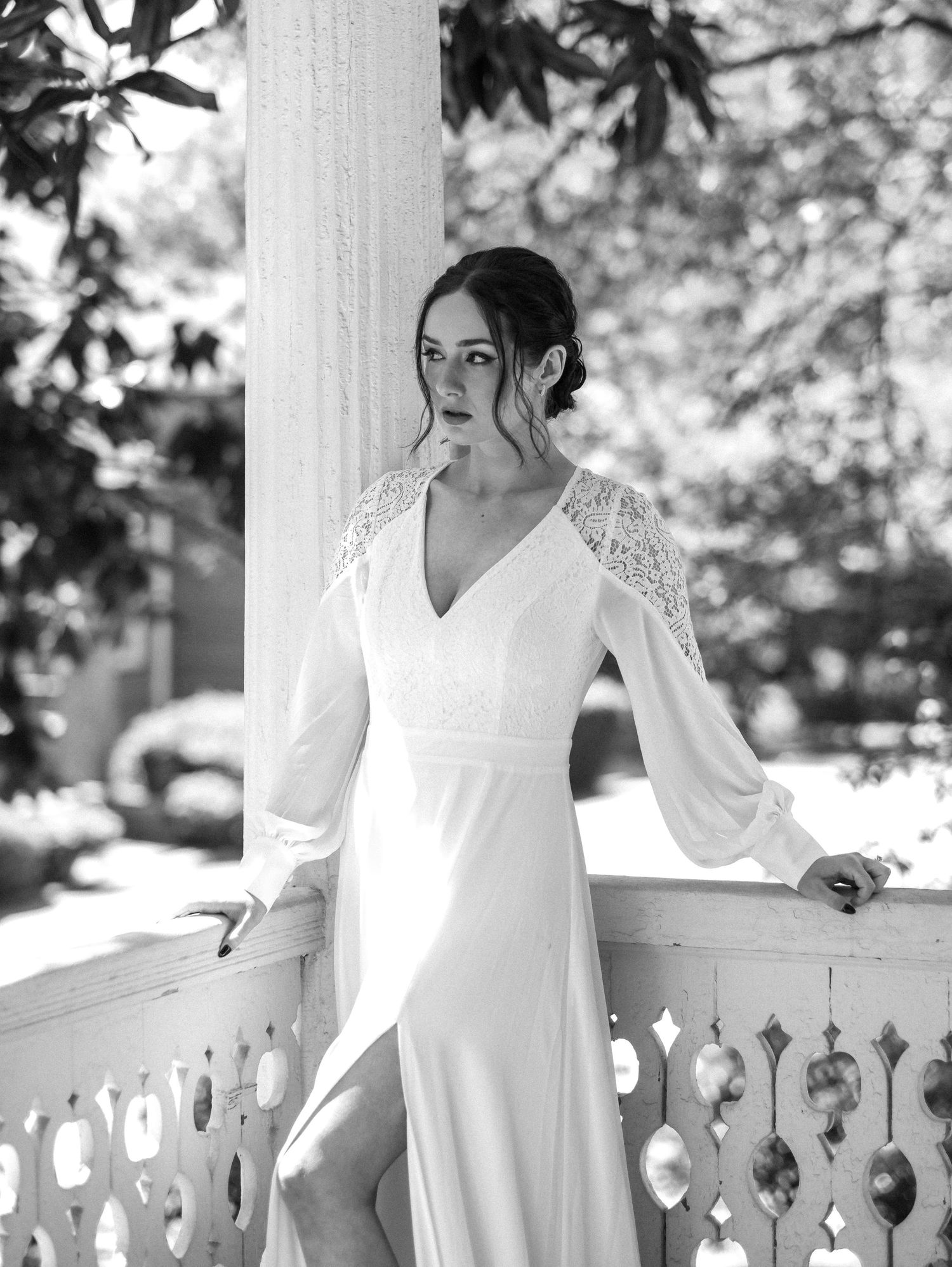 Classic black and white portrait of a bride on a white porch with ornate railings.