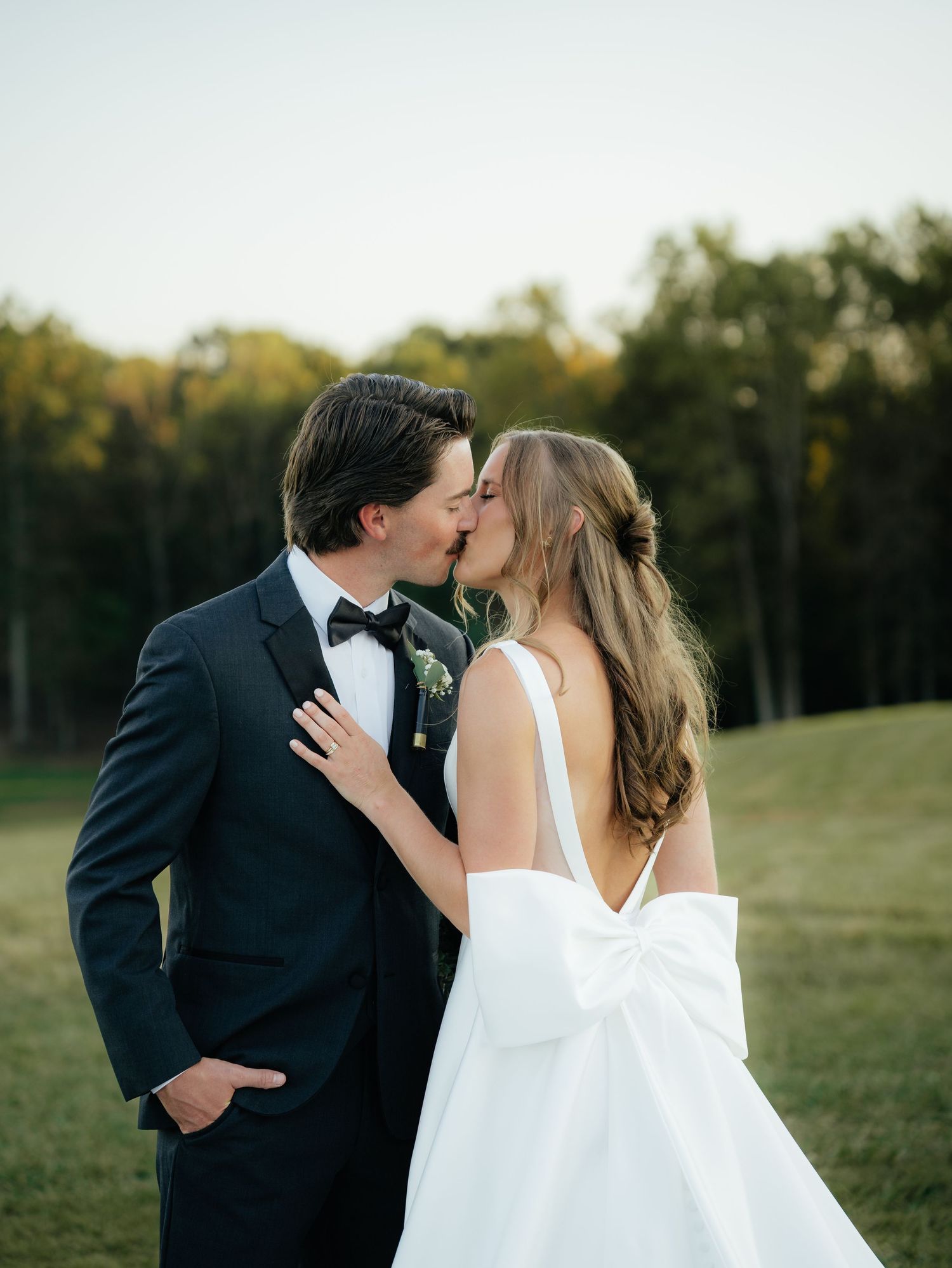 A romantic wedding couple shares intimate kisses in a series of photos taken in a scenic outdoor field at sunset.
