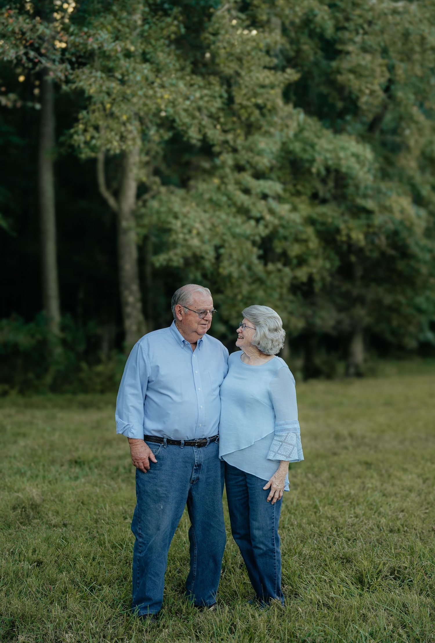 An endearing couple in matching blue outfits share a tender moment in a grassy field.