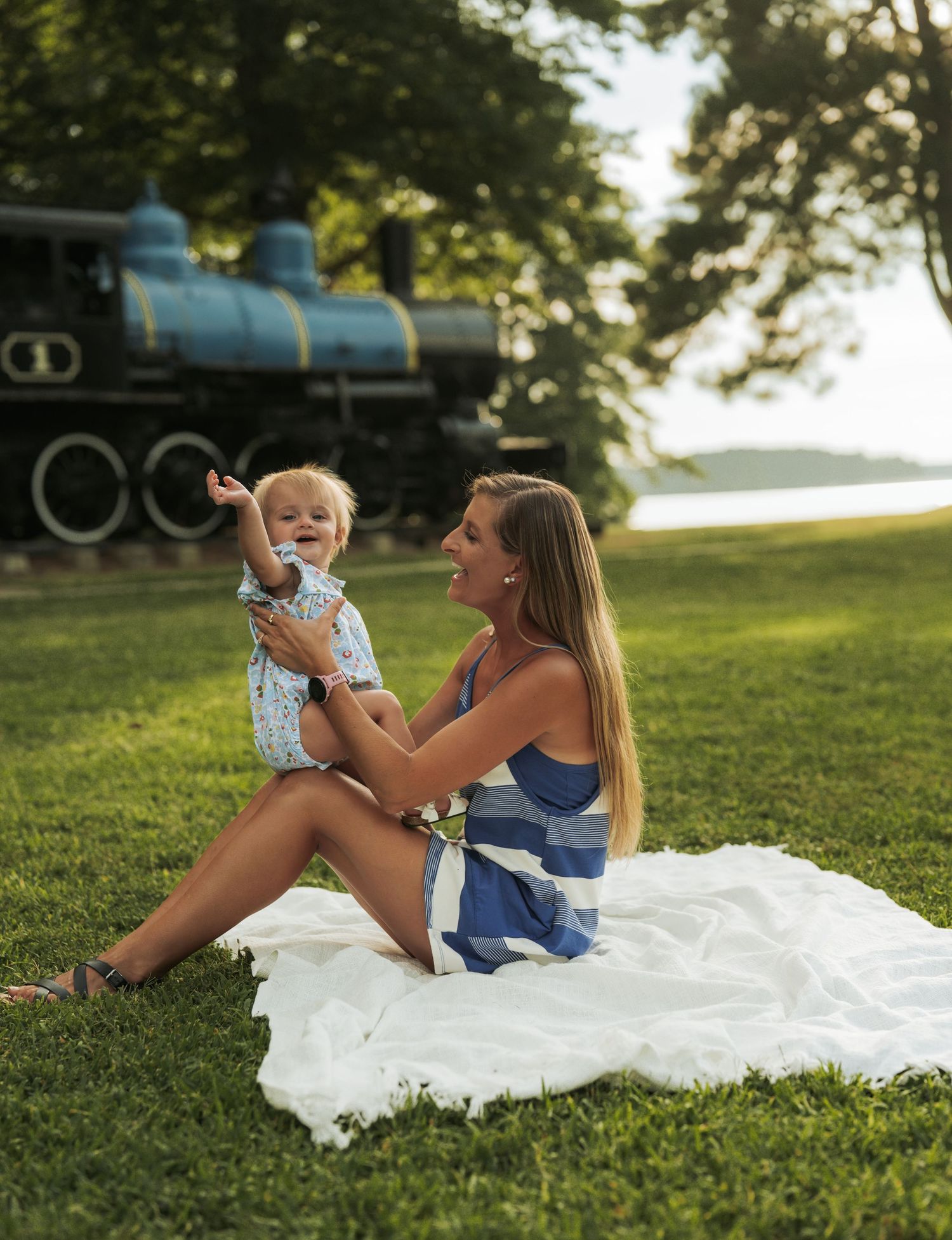Mother and baby playing on white blanket in park during golden hour.