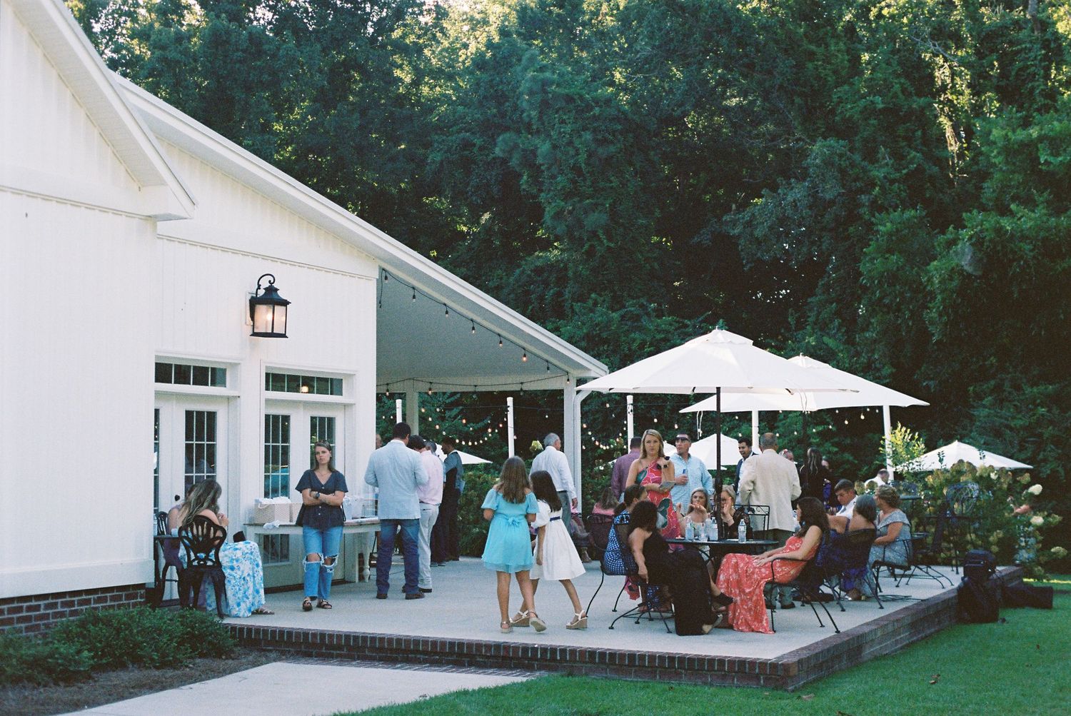 Wedding guests mingling on outdoor patio of white venue building.